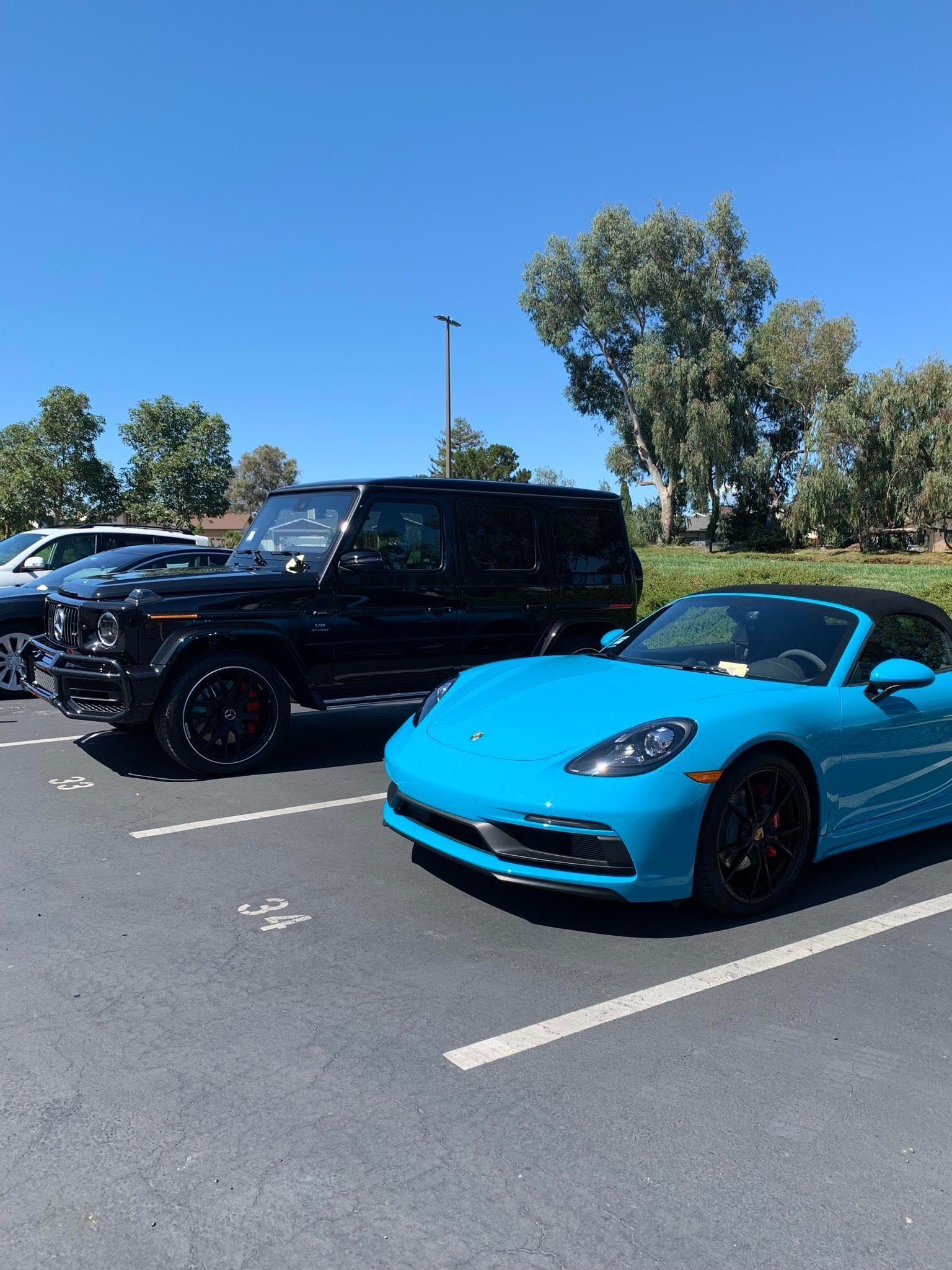 A blue sports car is parked next to a black suv in a parking lot.