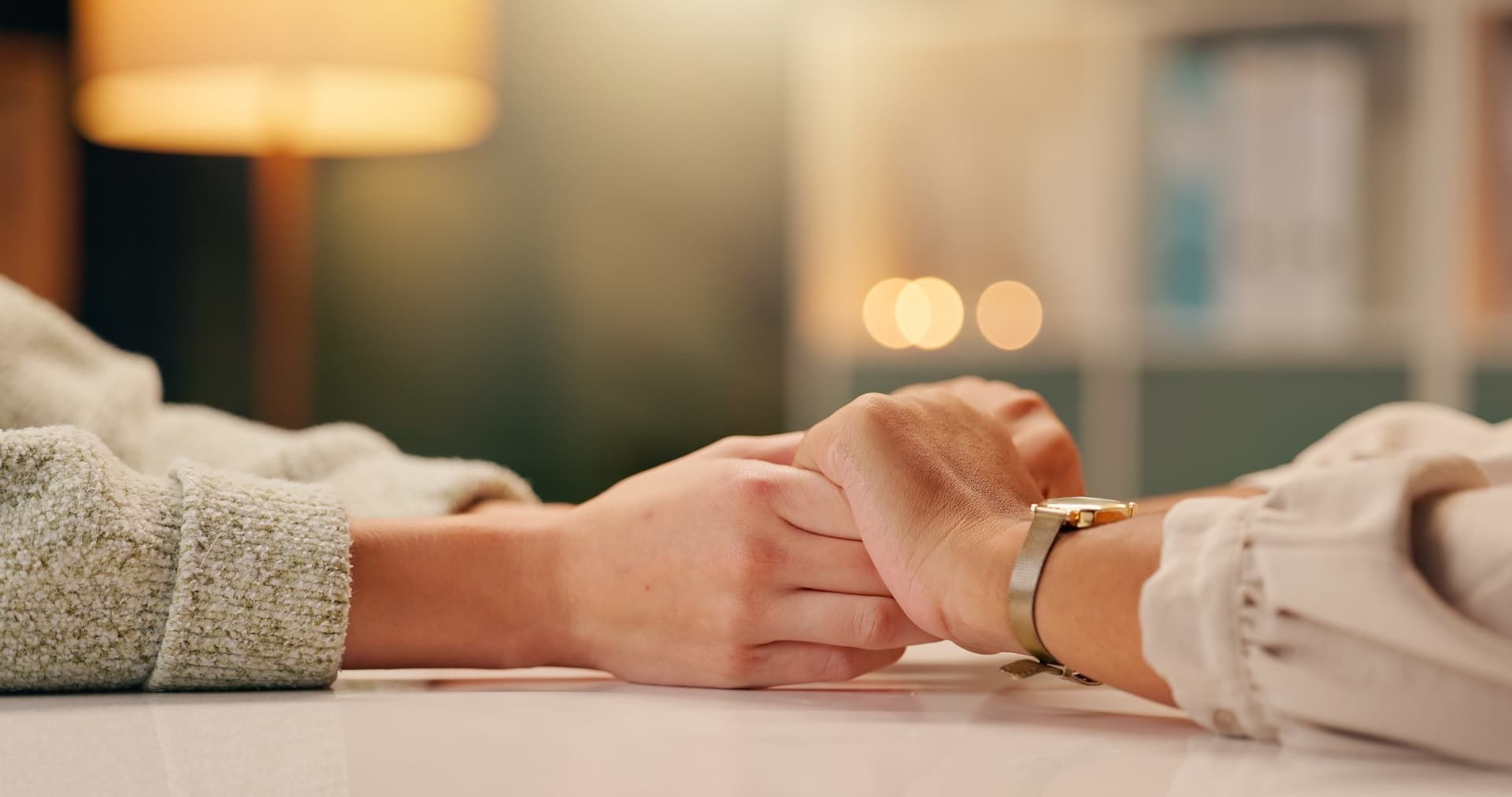 Two people holding hands across a table in a warm, softly lit room