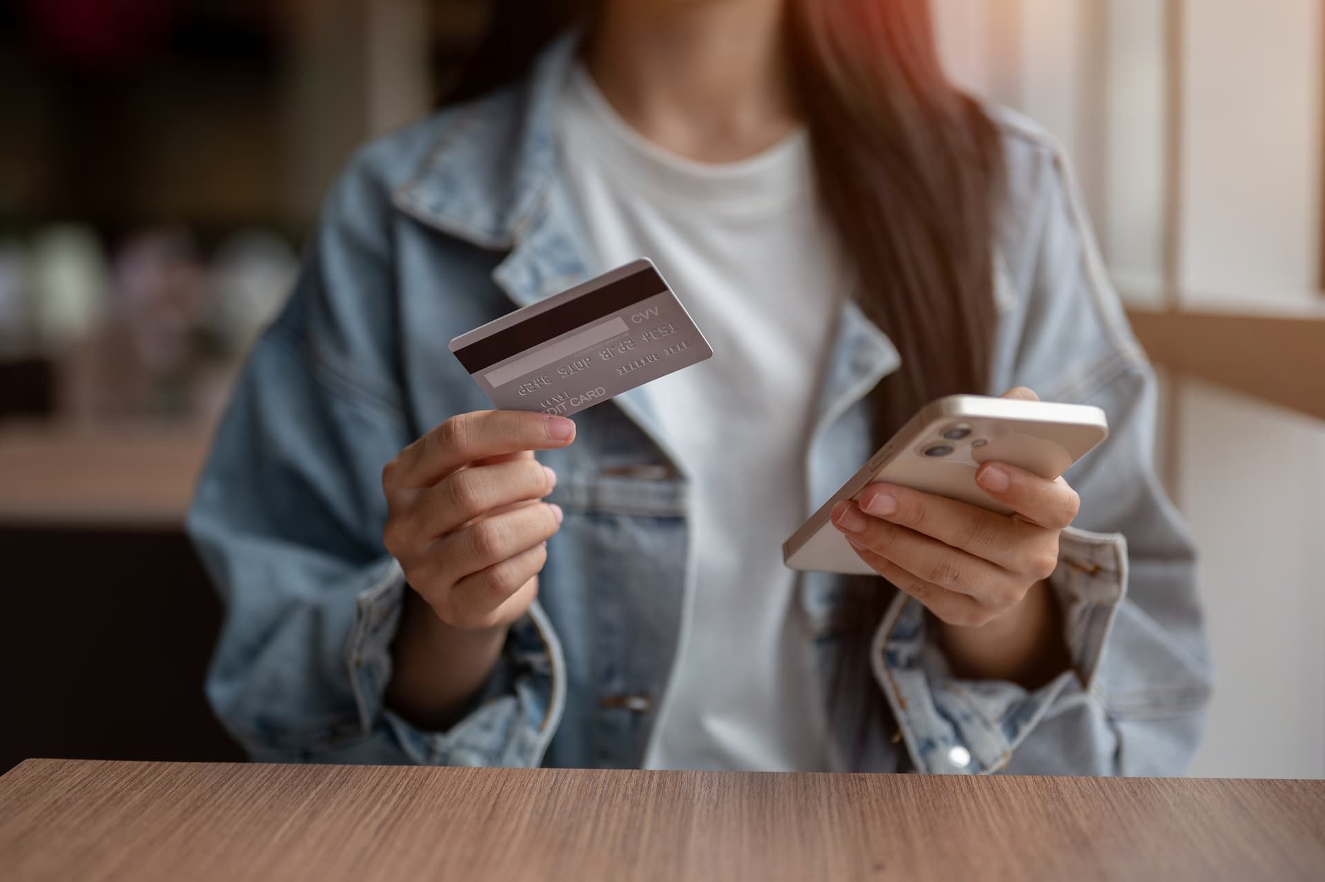 Person holding a credit card and smartphone at a table, suggesting online shopping or payment.