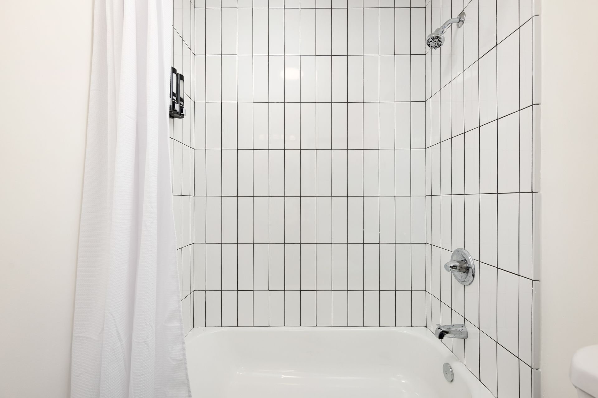 A bathroom shower area with white tile, a shower curtain, and a bathtub.
