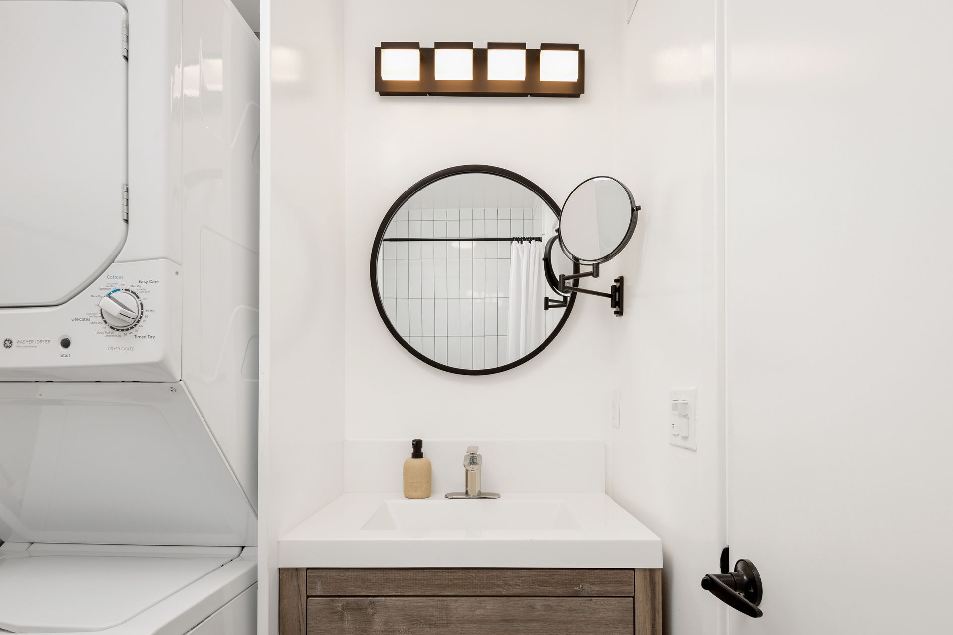 A bathroom sink with a round mirror and a stacked washer-dryer unit