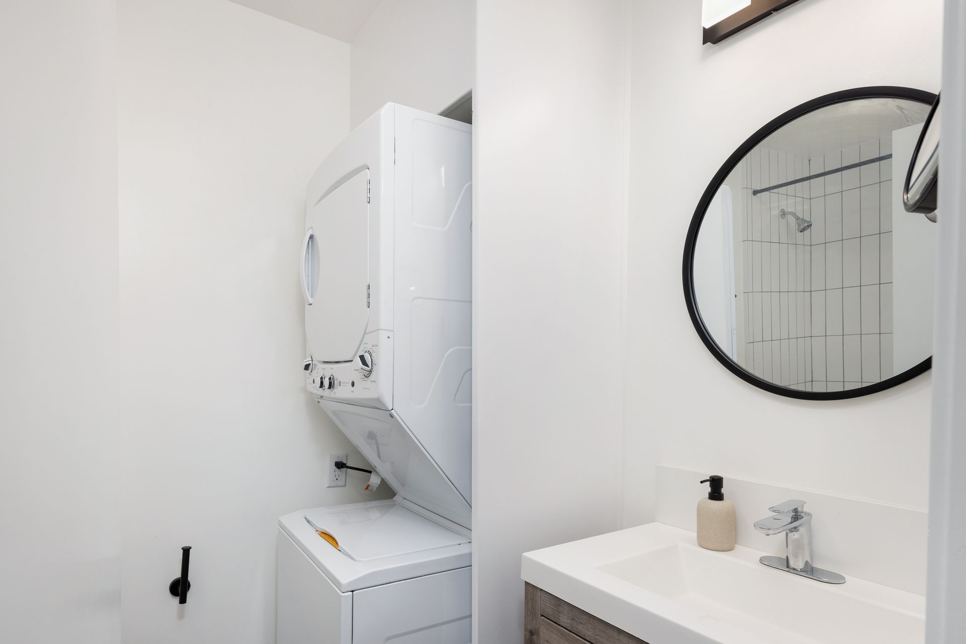 A bathroom with a washer/dryer, sink, and mirror