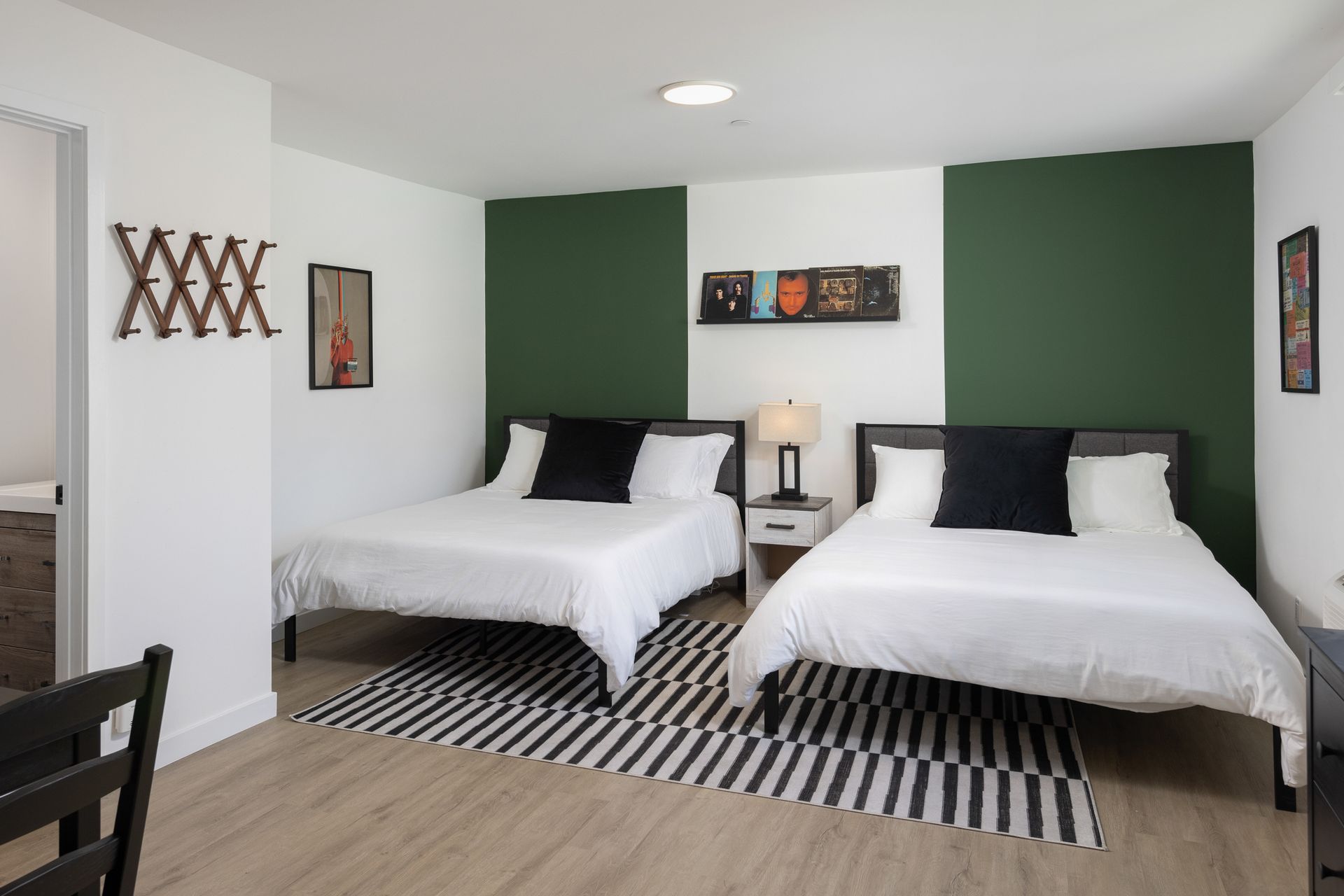 A hotel room with two queen beds, dark green accent walls, a striped area rug, and modern decor.