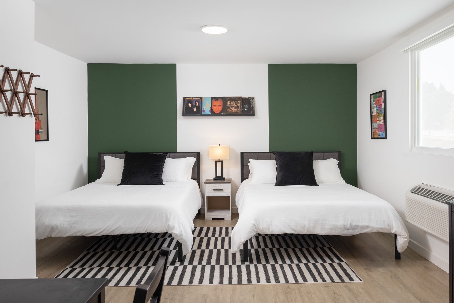 Hotel room with two beds, white bedding, black accent pillows, dark green wall panels, and a black and white striped rug.