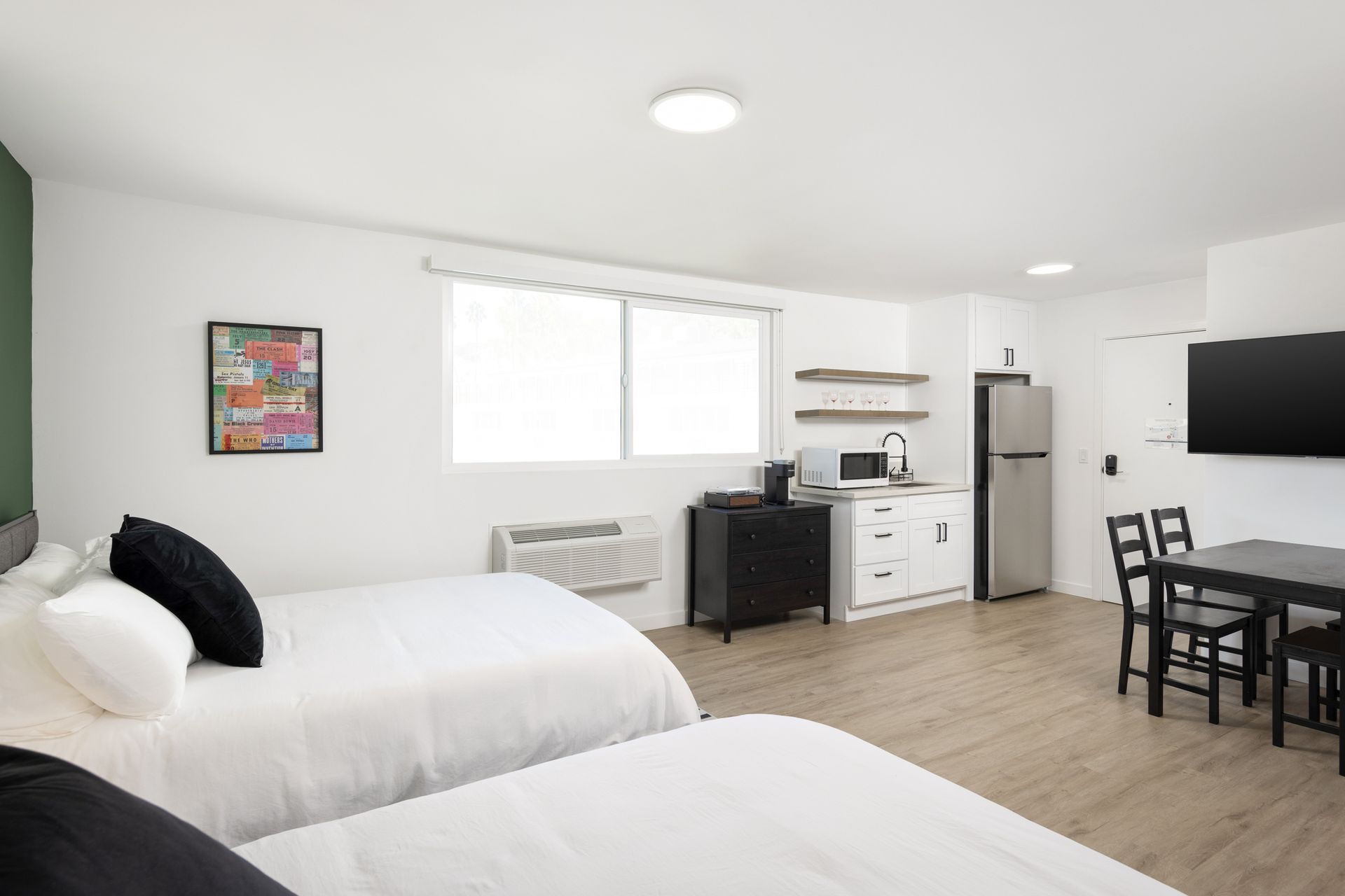 A bright and clean hotel room with two beds, a kitchenette, and a dining table.