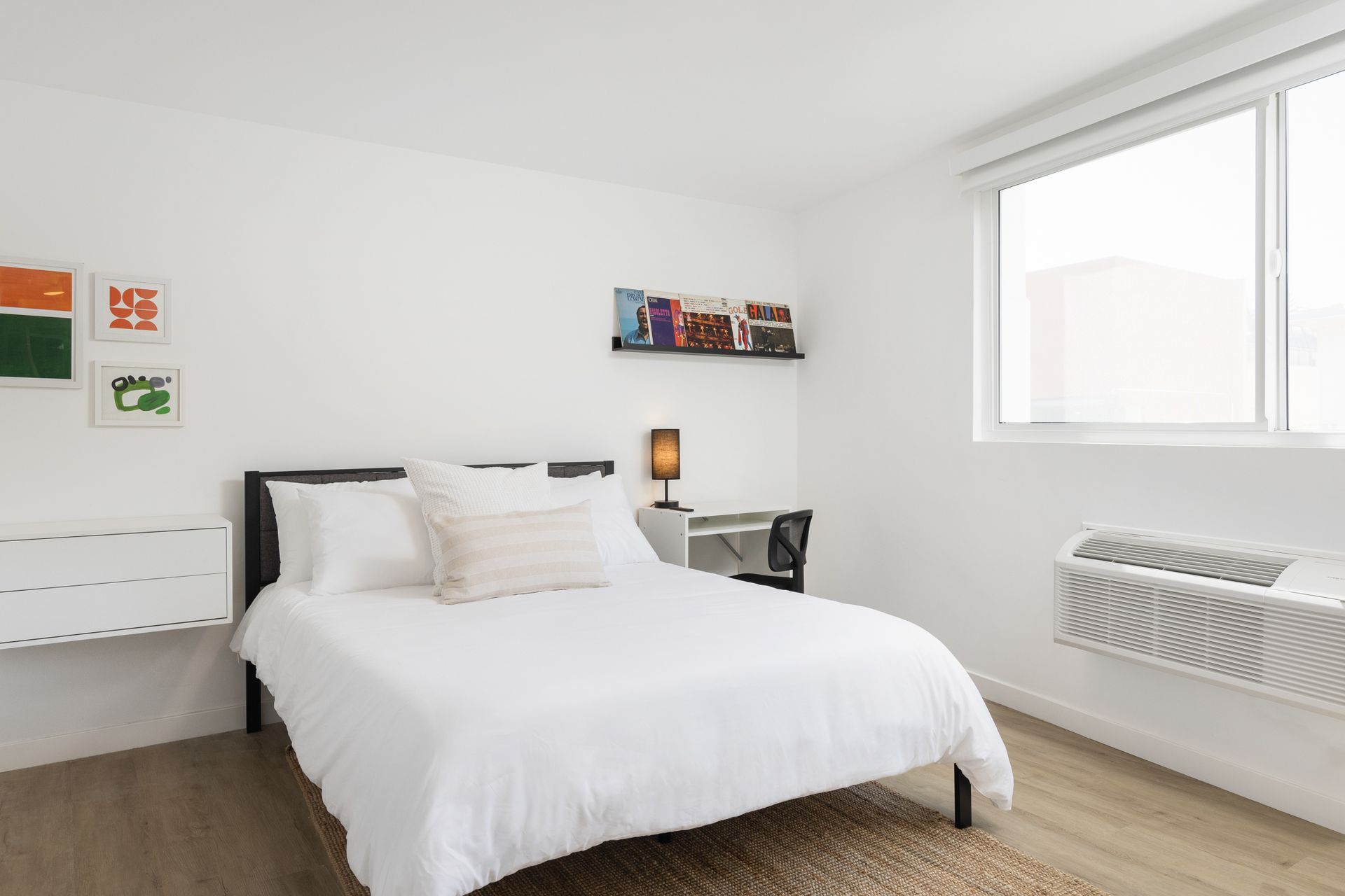 A clean and minimalist guest room with a bed, desk, and window