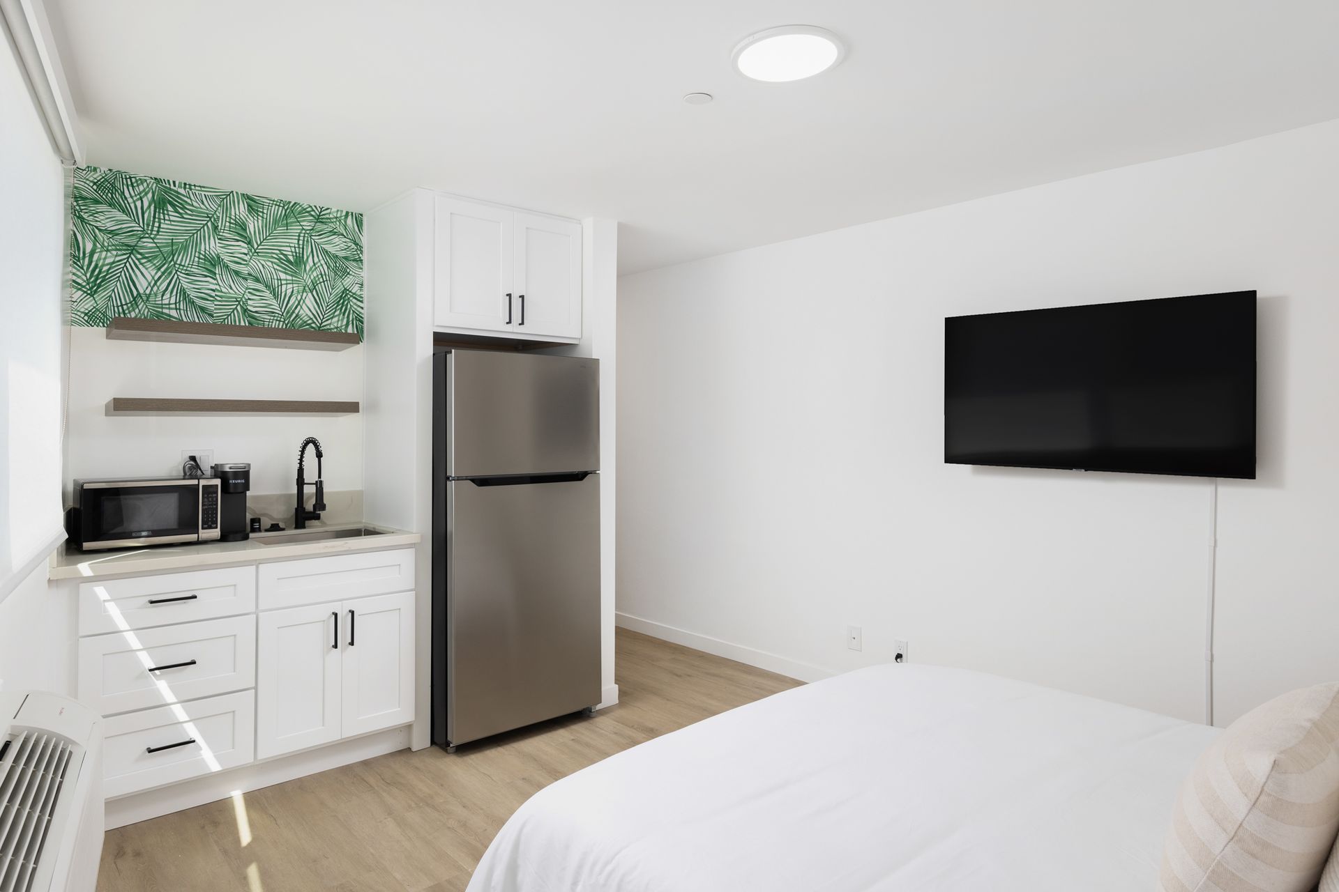 A compact hotel room with a kitchenette, bed, and TV