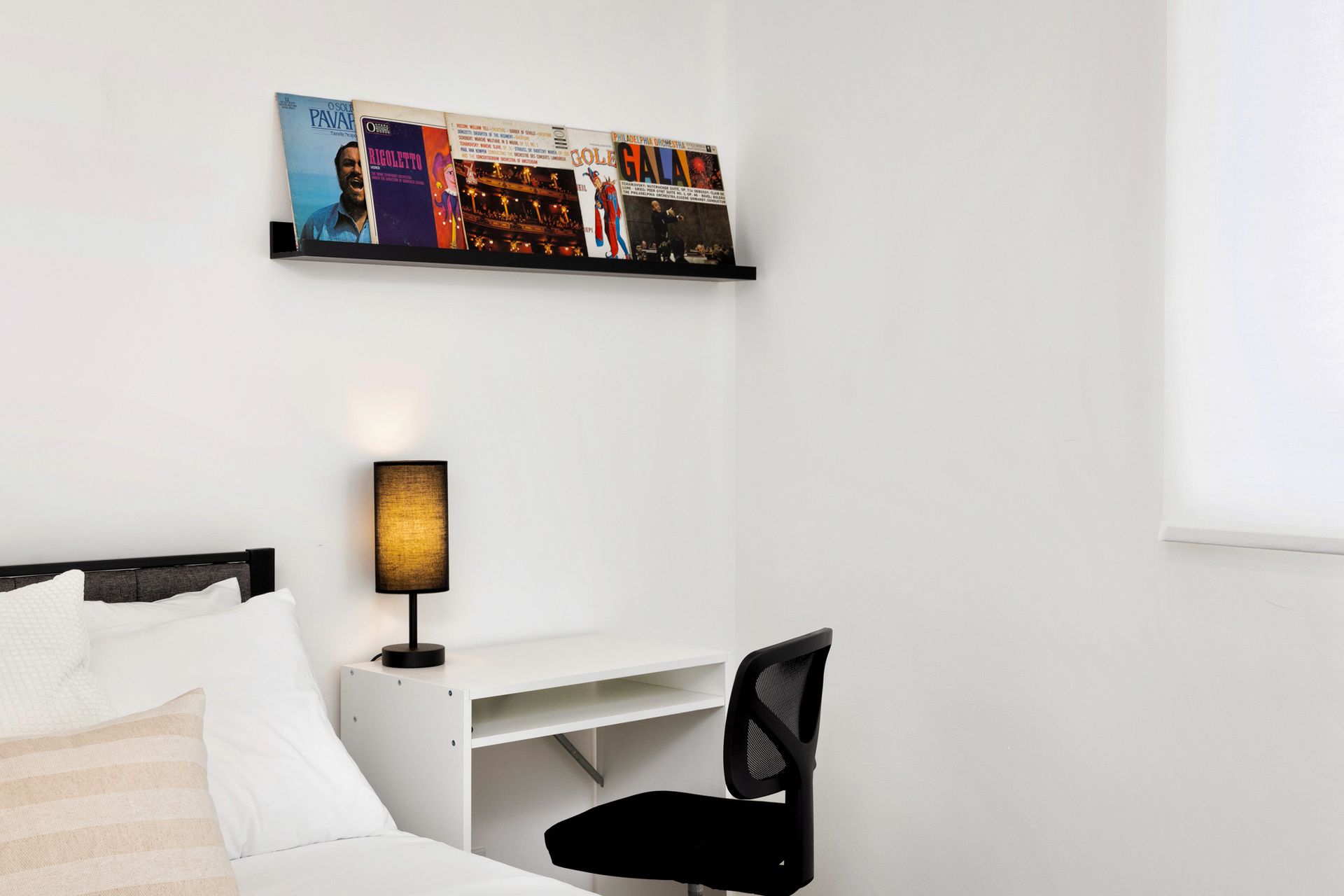 A hotel room with a bed, desk, chair, and lamp, featuring a vinyl record display.