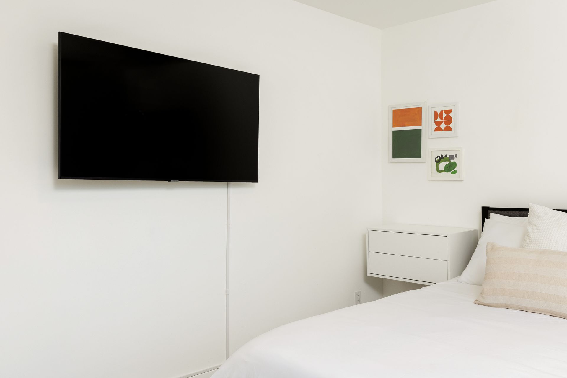 A white room with a bed, TV, and artwork.