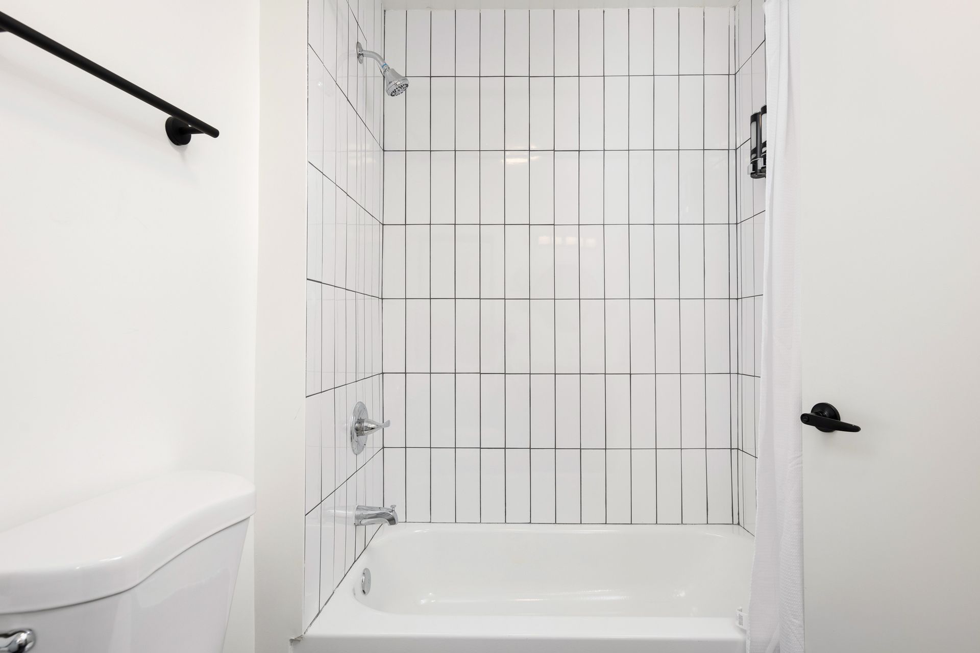 A bathroom with a white tub and shower, a toilet, and white tile