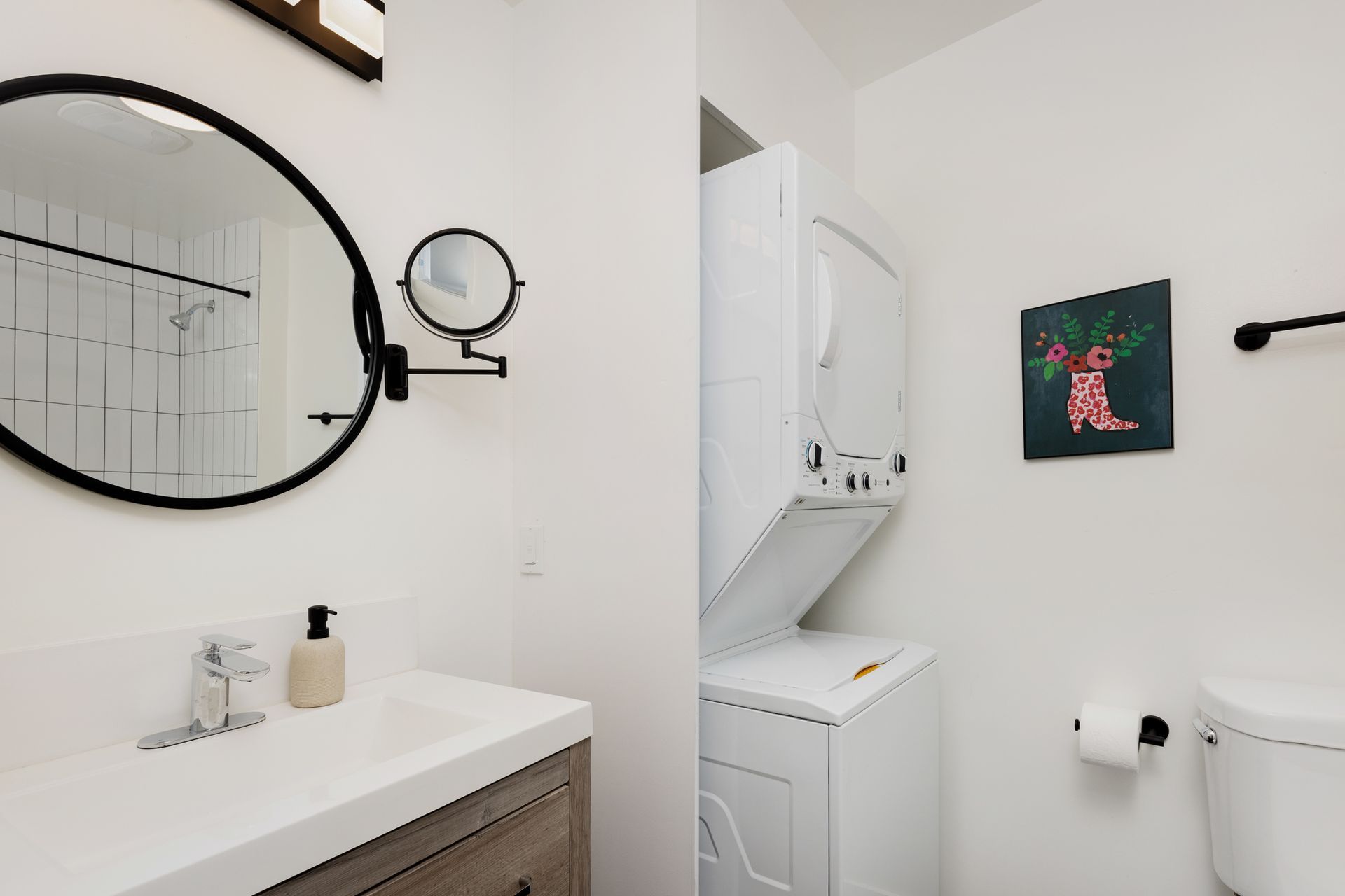 A bathroom with a sink, toilet, washer/dryer, and painting