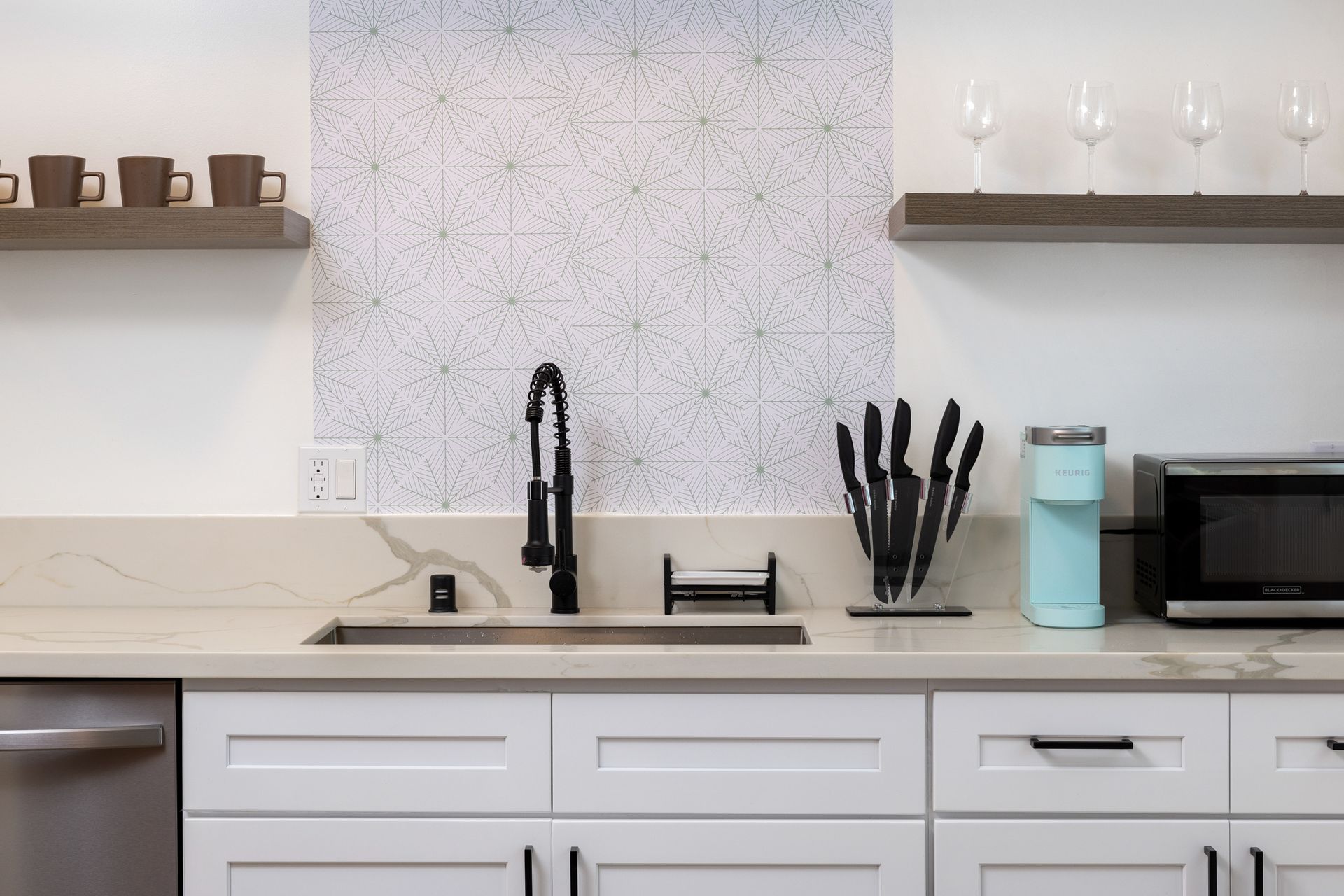A kitchenette with white cabinets, marble countertops, and modern appliances.