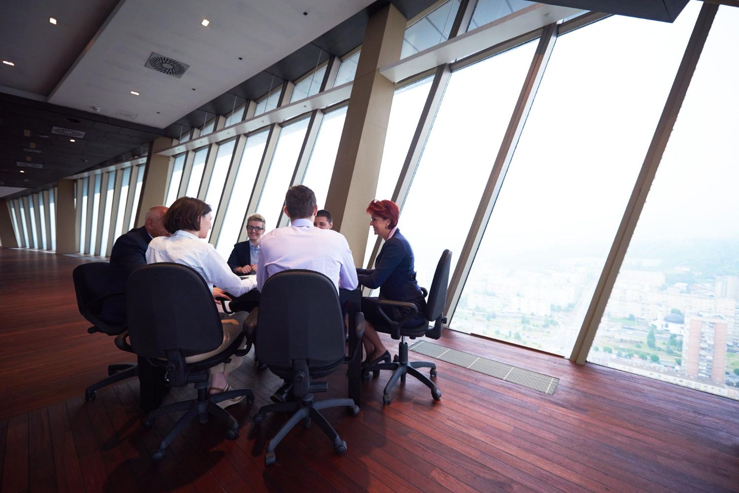 Business team in meeting at a high-rise, looking at paperwork, sunlight streaming through windows.