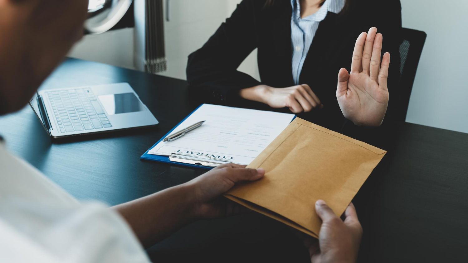 Person offering bribe to another, who is refusing with a raised hand.