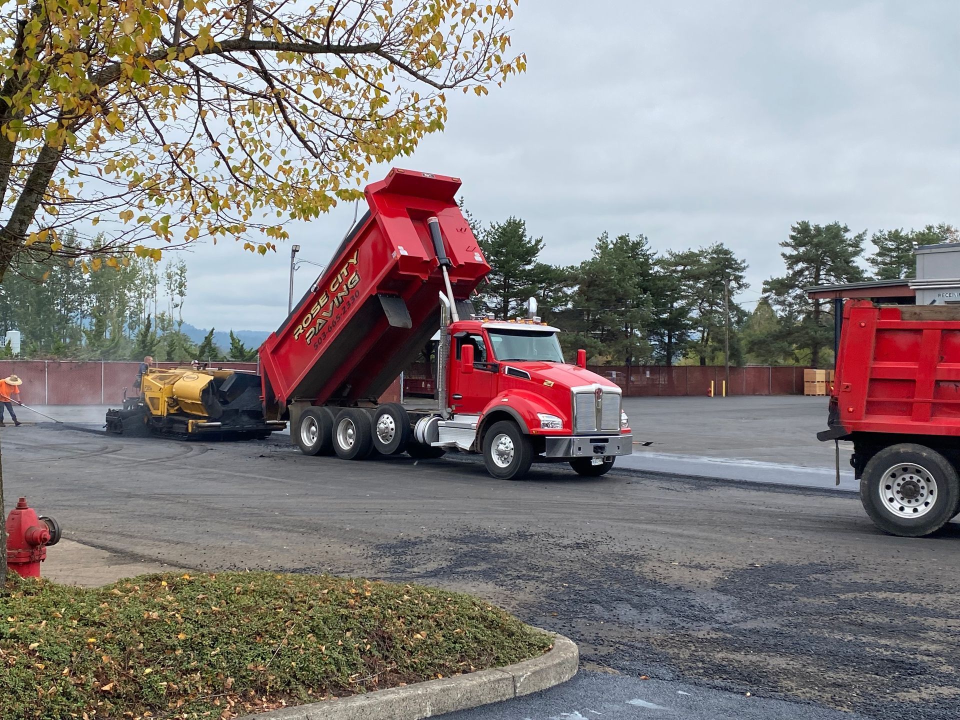 Red dump truck unloading asphalt for paving machine on a parking lot.