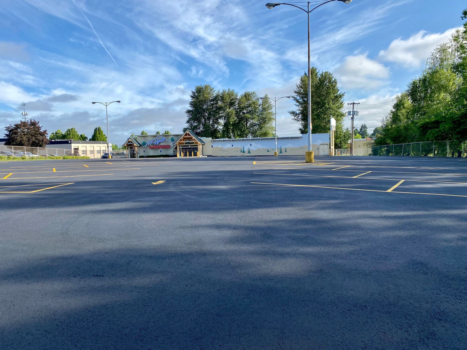 Empty asphalt parking lot in front of a long, single-story commercial building under a partly cloudy sky.