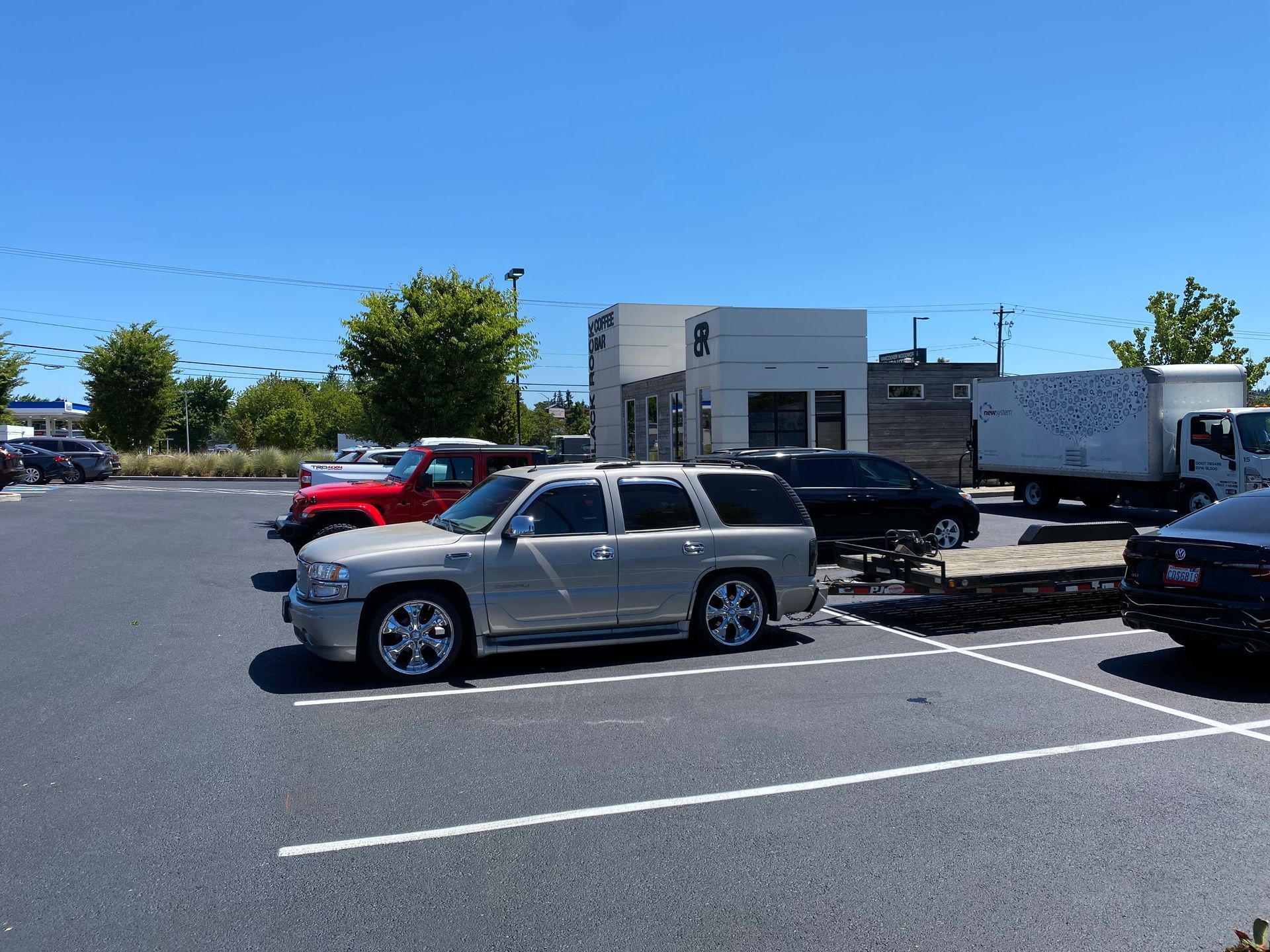 Silver SUV parked in a lot, other cars and a small building in the background on a sunny day.