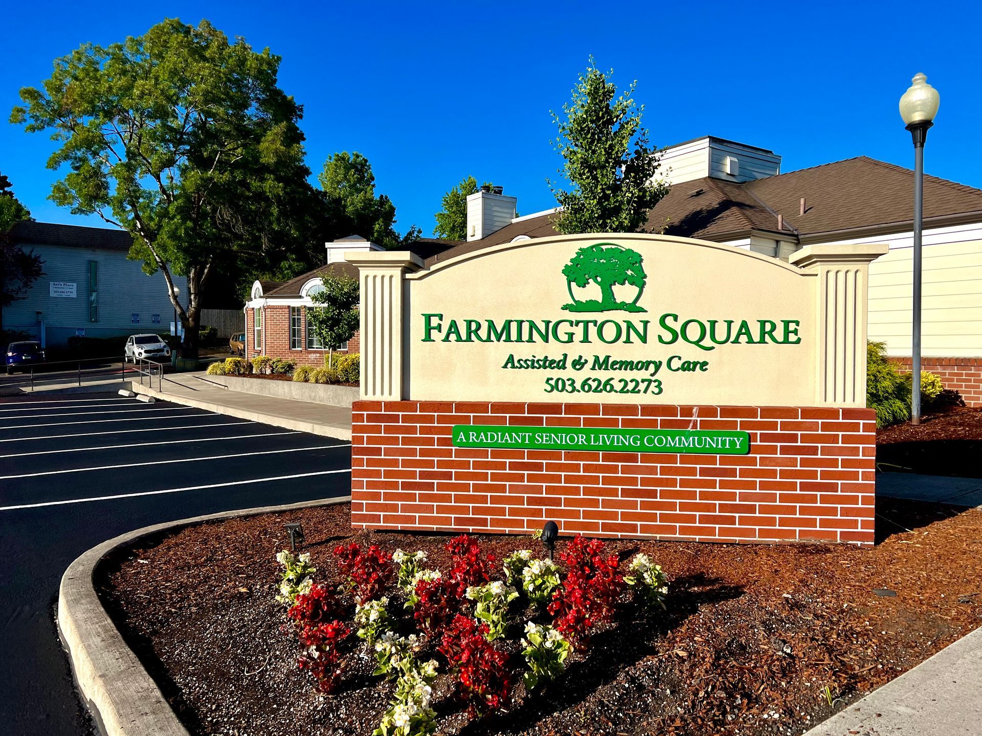 Sign for Farmington Square Assisted & Memory Care. Building in background, red brick and flowers in front.