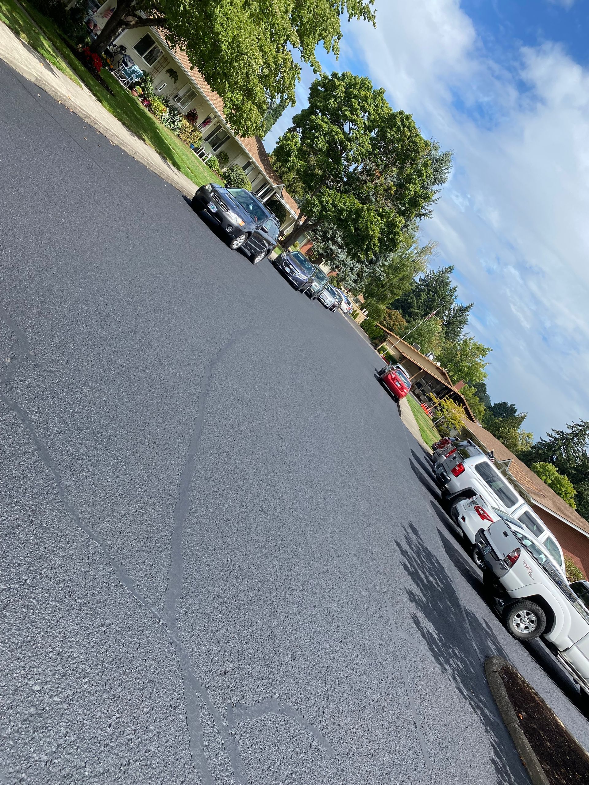 Newly paved street with parked cars on both sides under a blue sky with trees.