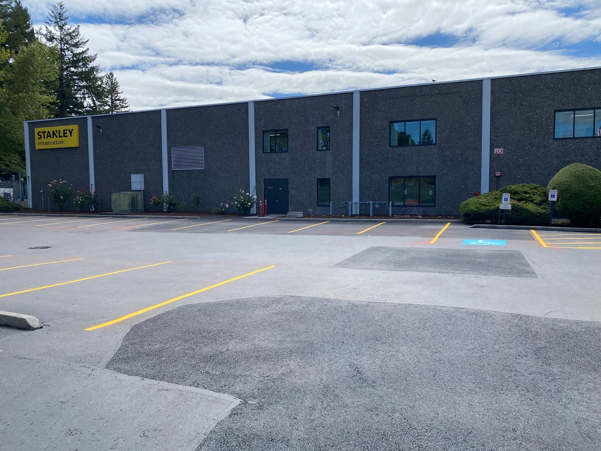 Parking lot in front of a gray building with yellow signage, a flag, and marked parking spaces.