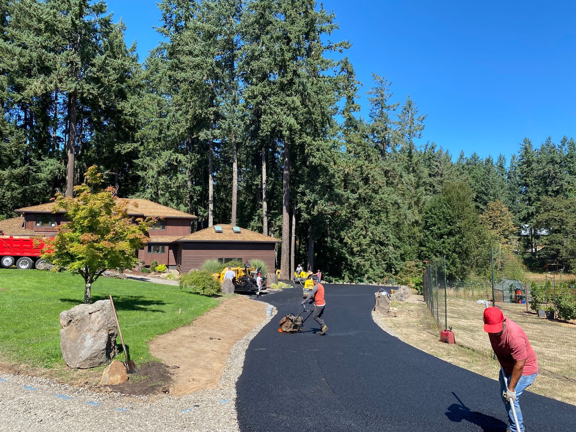 Asphalt driveway being paved, crew working near a home, trees in the background.