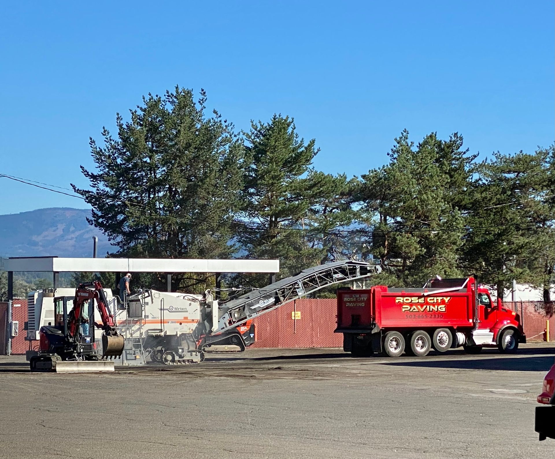 Road milling equipment and dump truck removing asphalt on a sunny day.