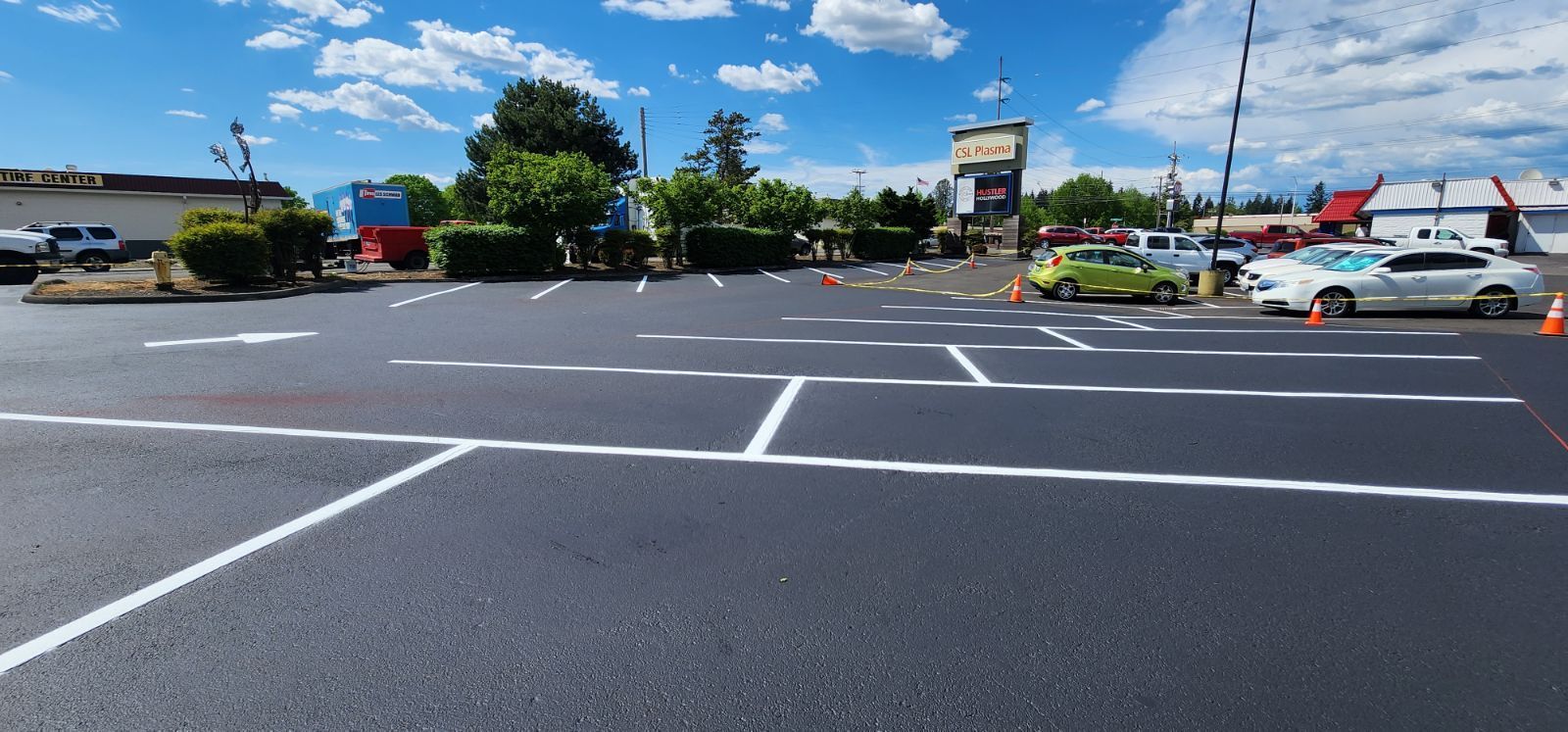 Parking lot with white lines, orange cones, and parked cars under a blue sky.