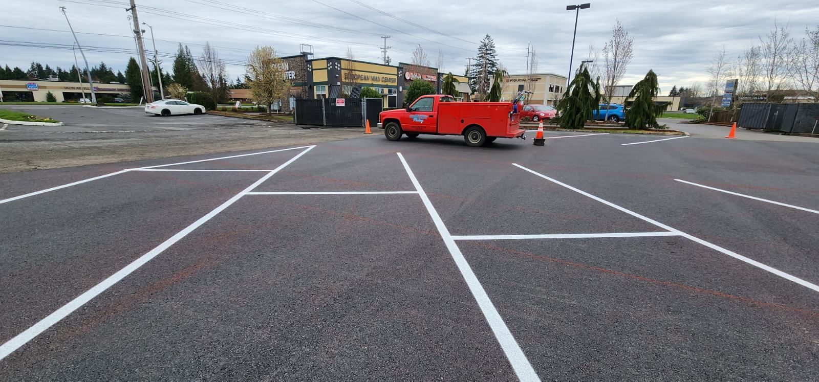 A red truck is parked in a newly painted parking lot. Cloudy sky, building in the background.
