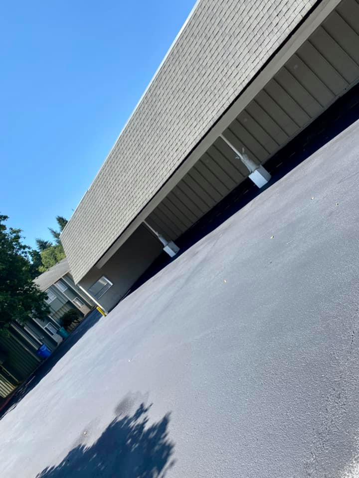 Long, sloped, gray building with dark asphalt below, a blue sky above.
