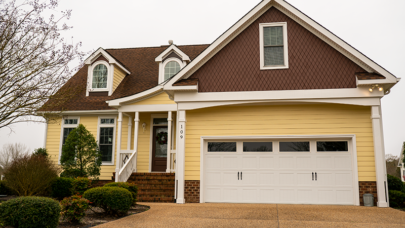 Suburban house with brown siding, white trim, and a two-car garage under a cloudy sky