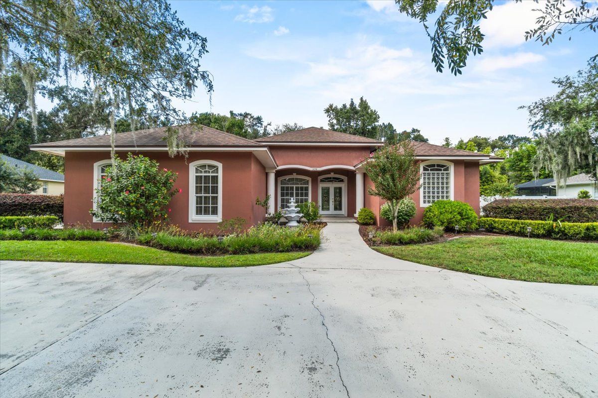 Single-story red brick house with white trim, arched entry, and a circular driveway surrounded by greenery