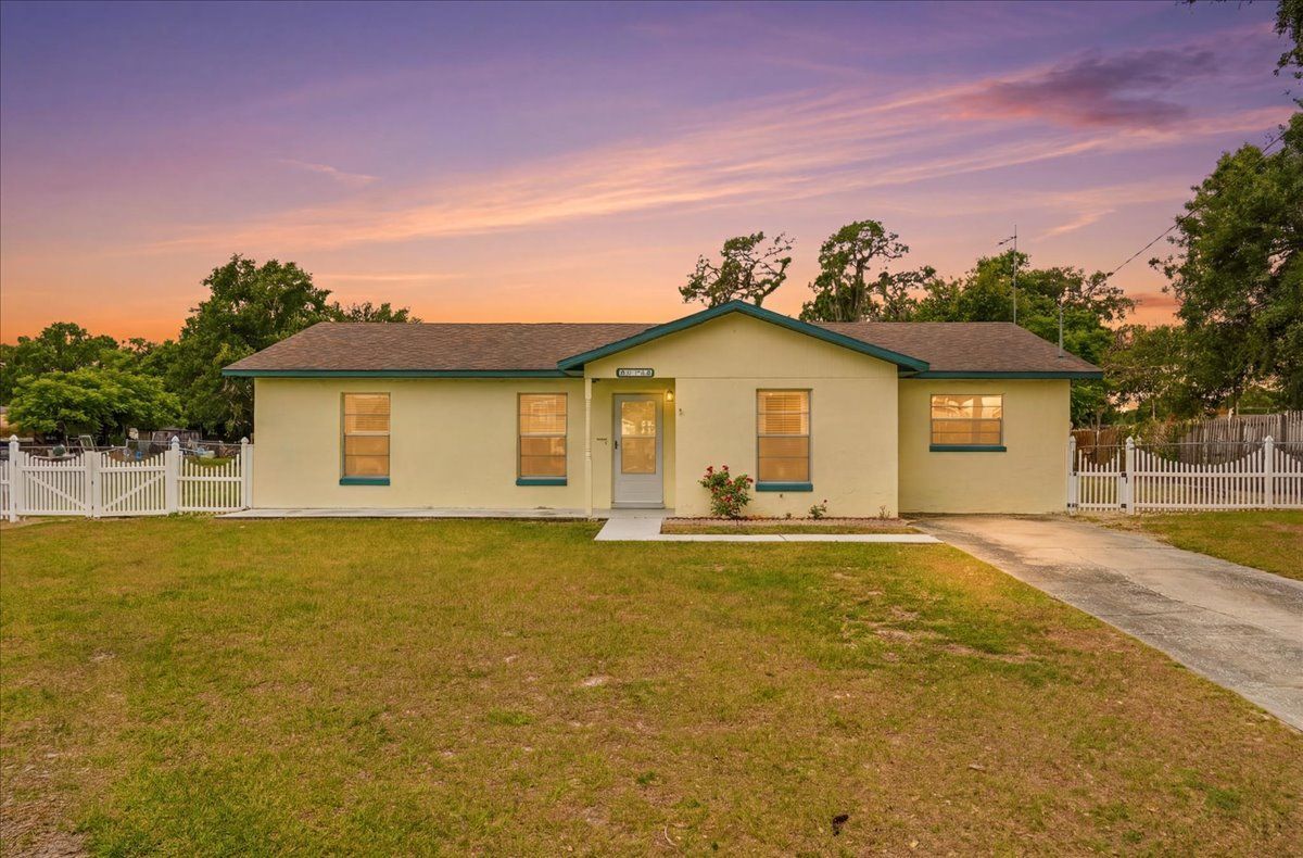 Single-story beige house with a front lawn and driveway at sunset