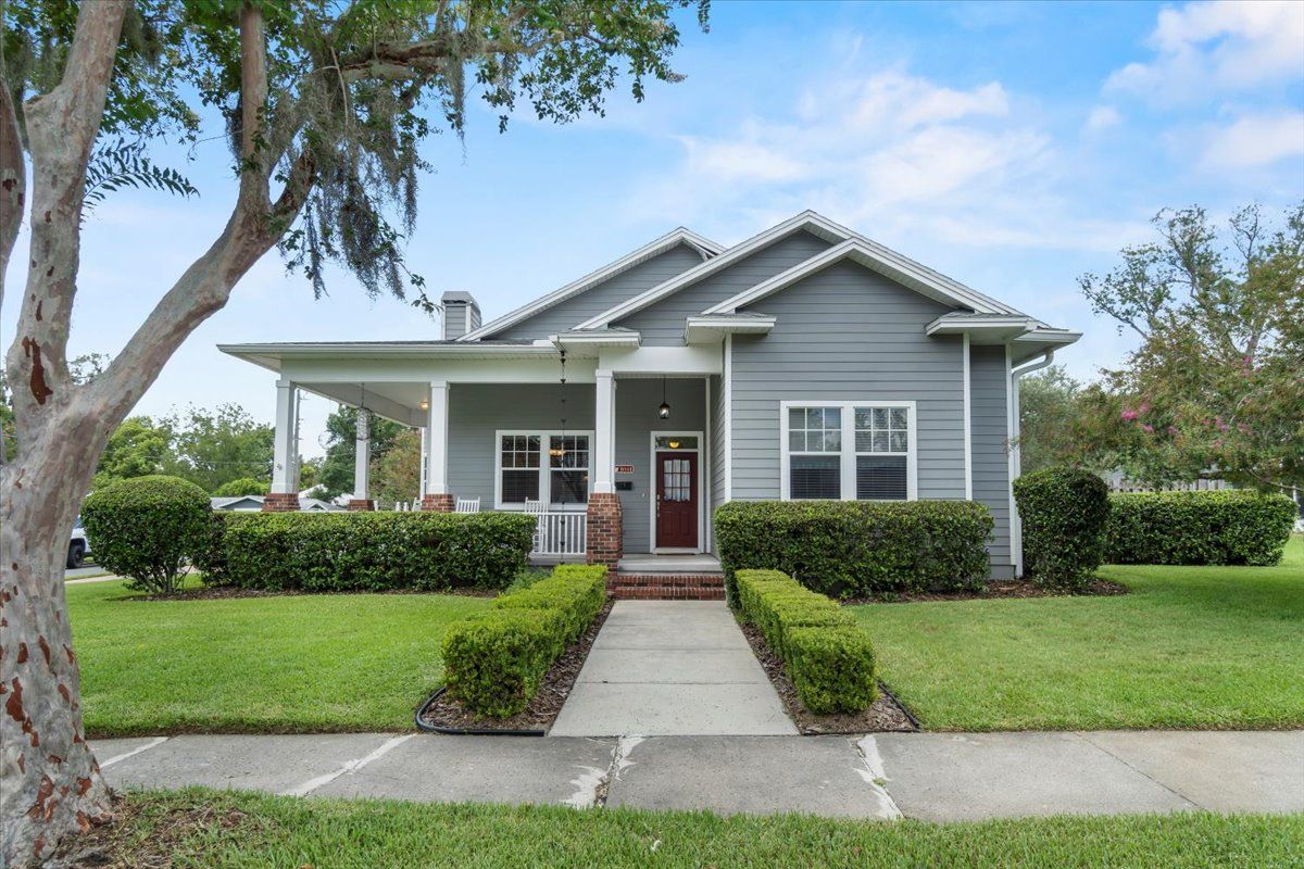 Gray house with a front porch, red door, and manicured lawn under a blue sky