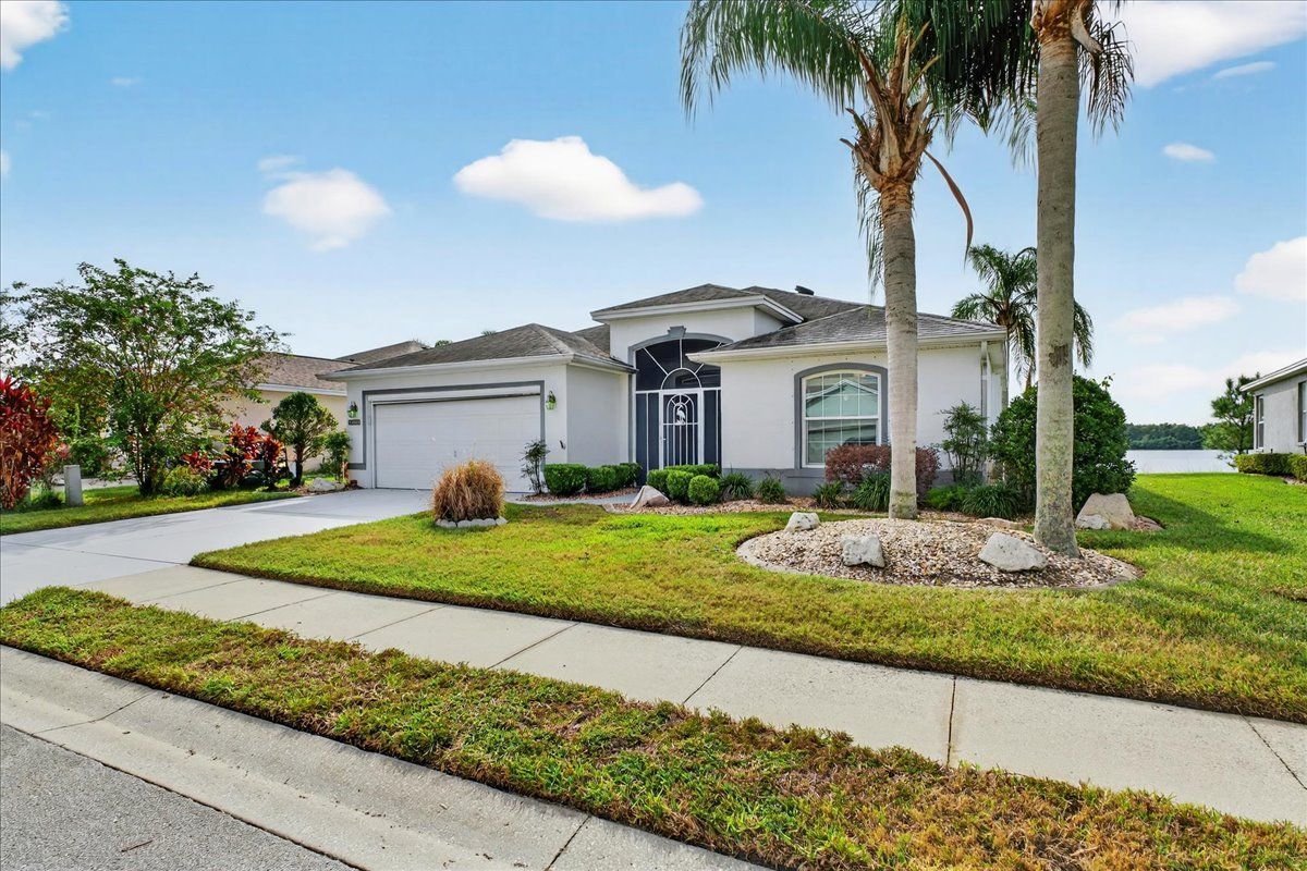 Modern white suburban house with manicured lawn, palm trees, and a curved driveway under a blue sky