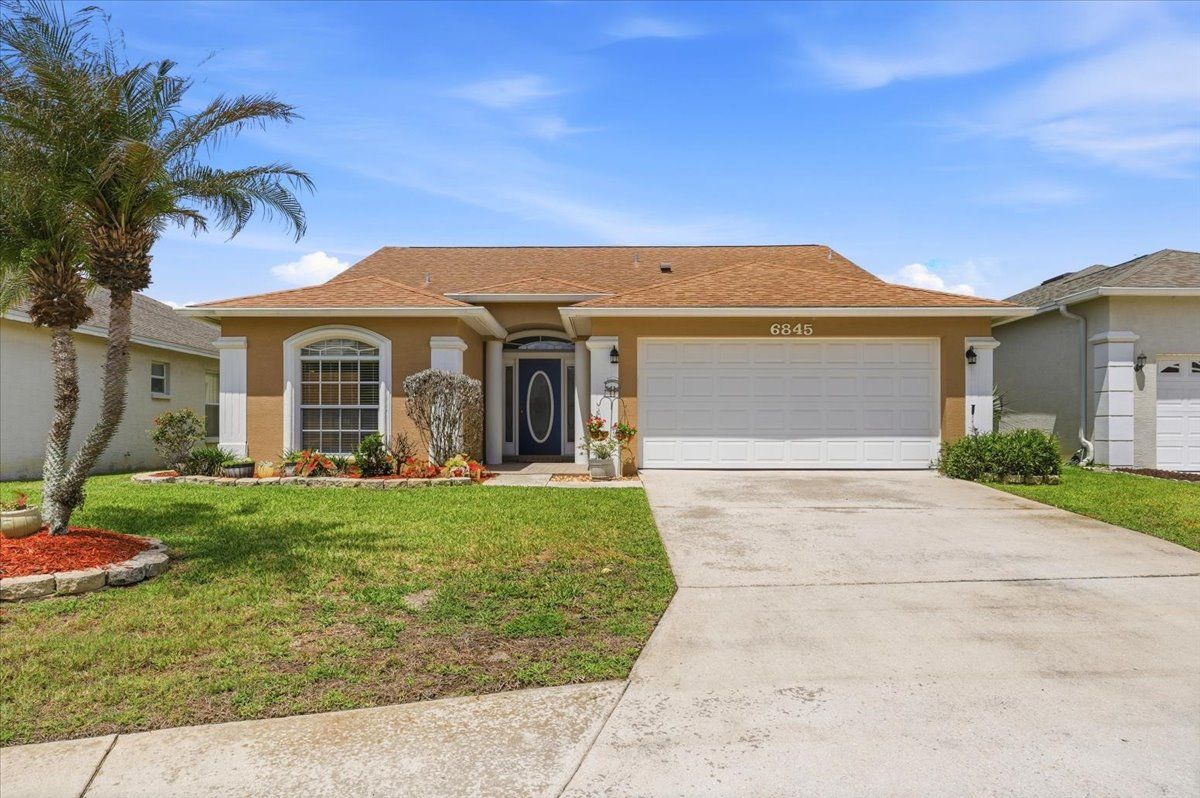 Single-story suburban house with a two-car garage, driveway, and front lawn under a clear sky