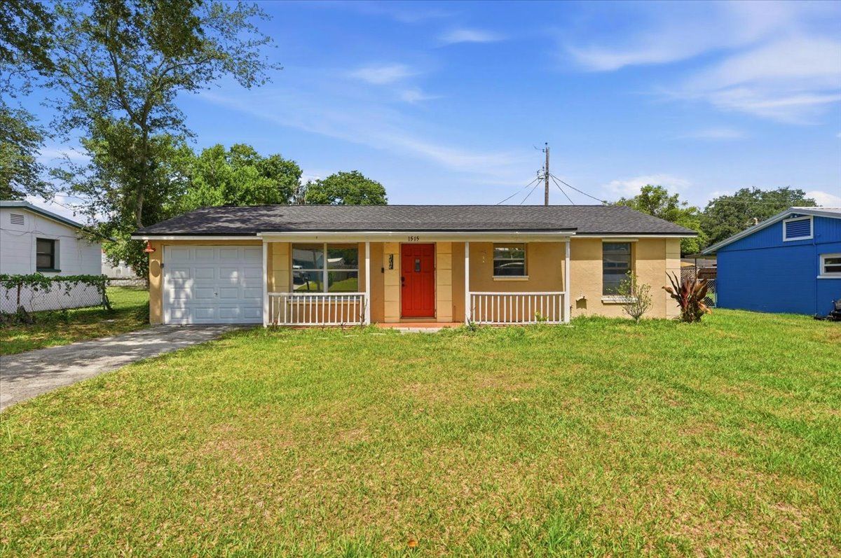 Single-story beige house with a red front door and a large grassy yard under a blue sky