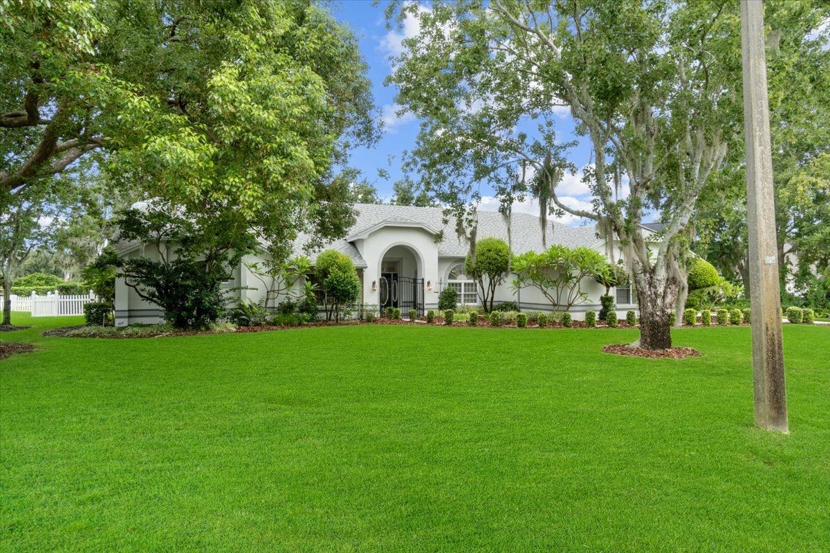 White house with arched entryway behind a large green lawn and trees under a blue sky