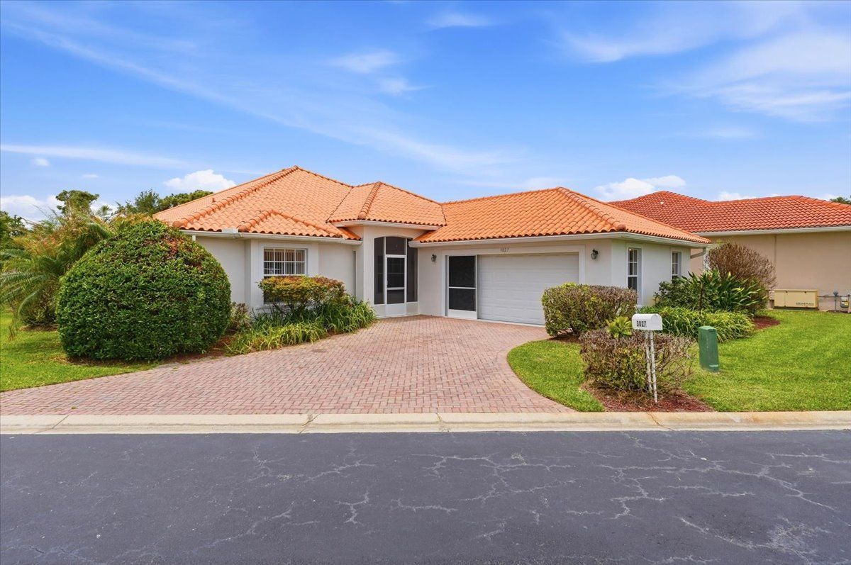 Single-story house with terracotta roof, white exterior, driveway, and green lawn under a blue sky