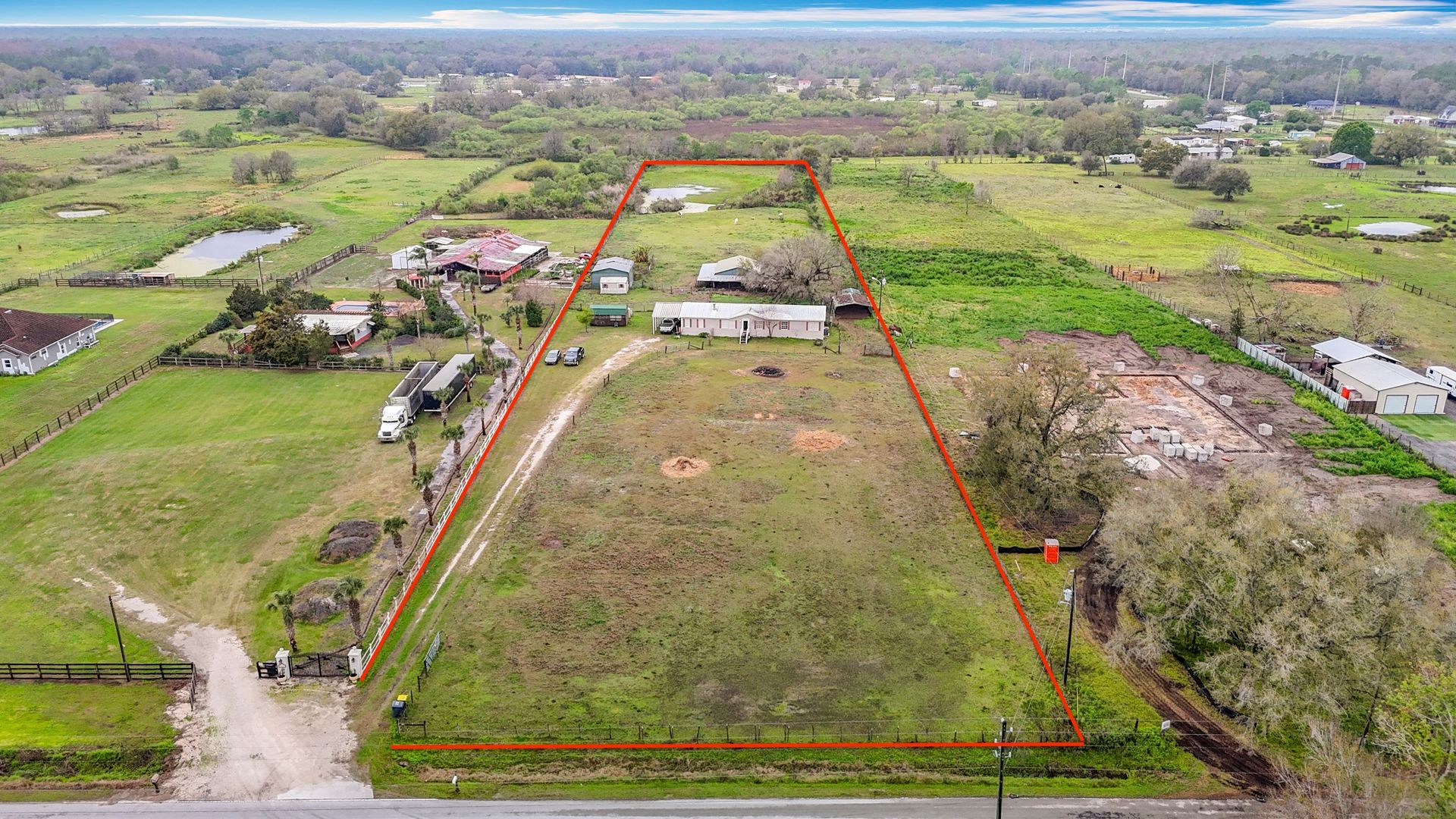 Aerial view of a large rural property outlined in red, with a house and open fields surrounded by trees.