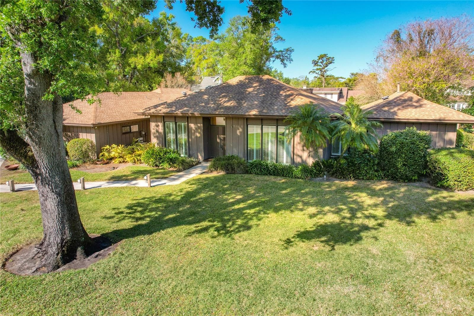 Single-story suburban house with a front lawn, trees, and landscaping on a sunny day