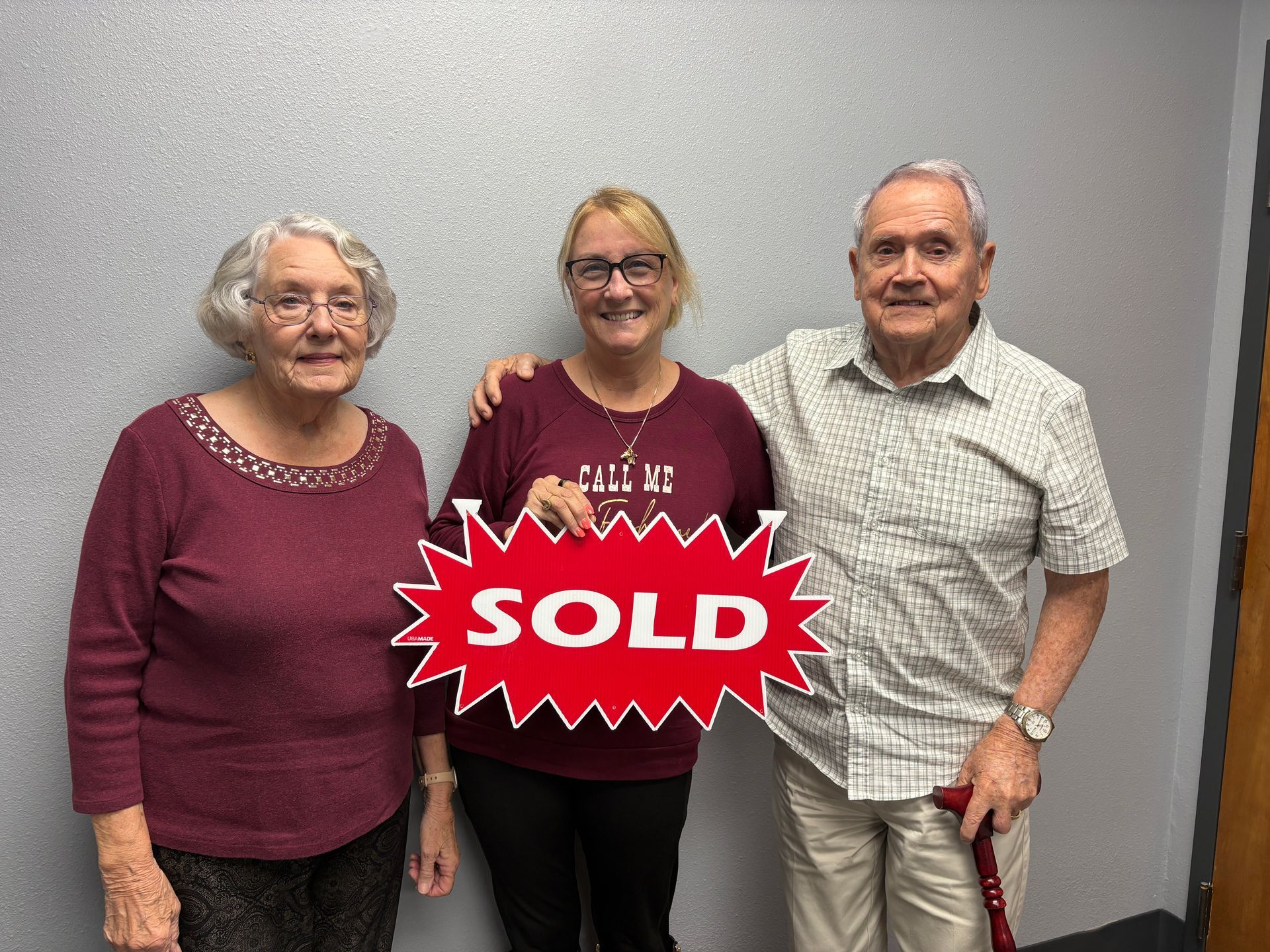 Three people standing indoors with a red “SOLD” sign in front