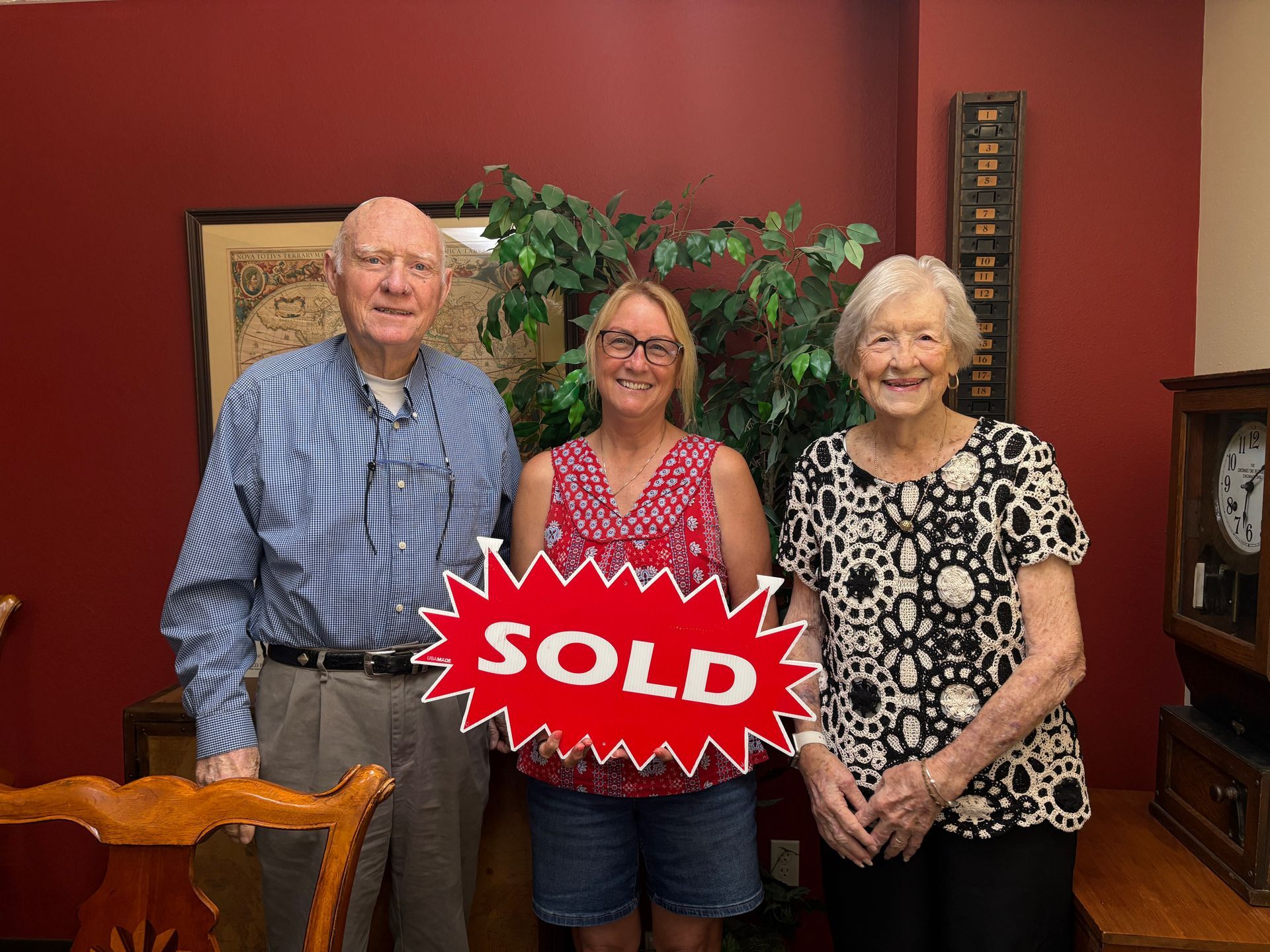 Three people standing indoors behind a red “SOLD” sign