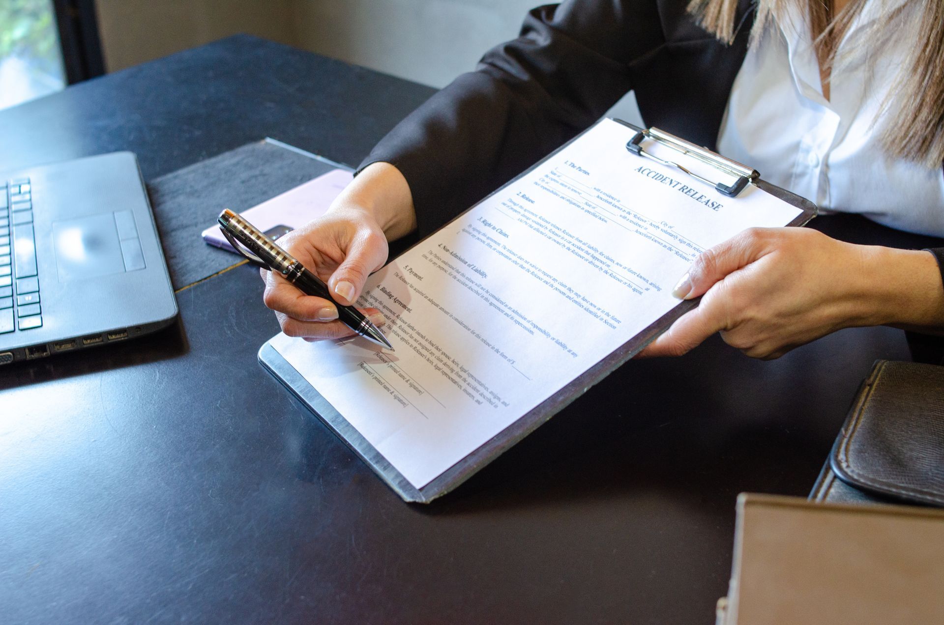 Hands signing a document on a clipboard at a desk next to a laptop