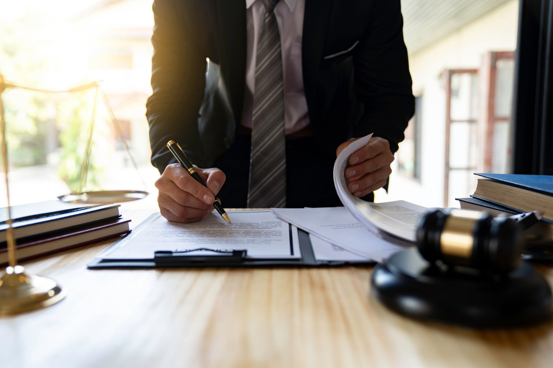 Person signing legal documents at a desk with a gavel in the foreground