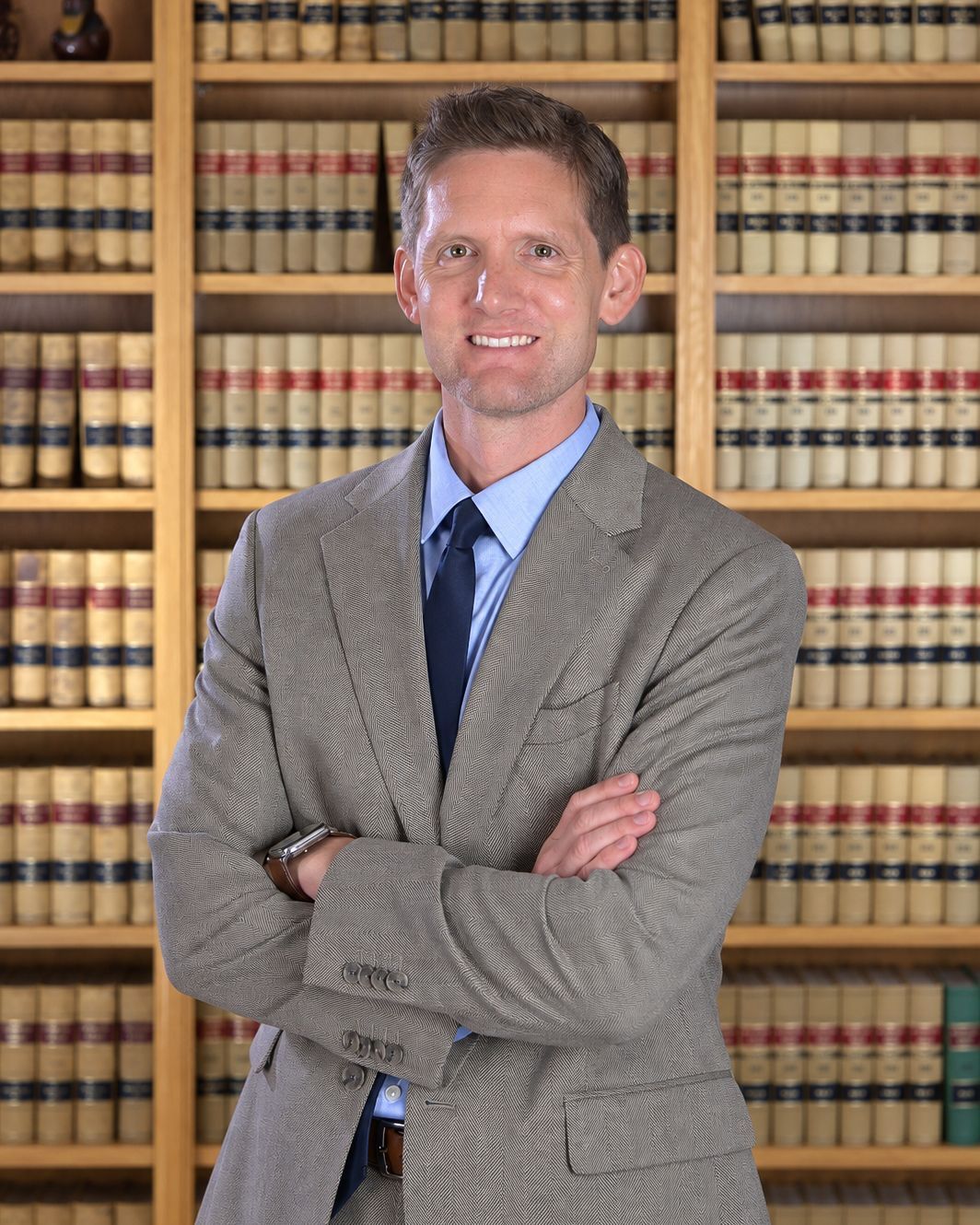Studio portrait of a smiling man in a dark suit, blue tie, and plaid shirt against a teal backdrop