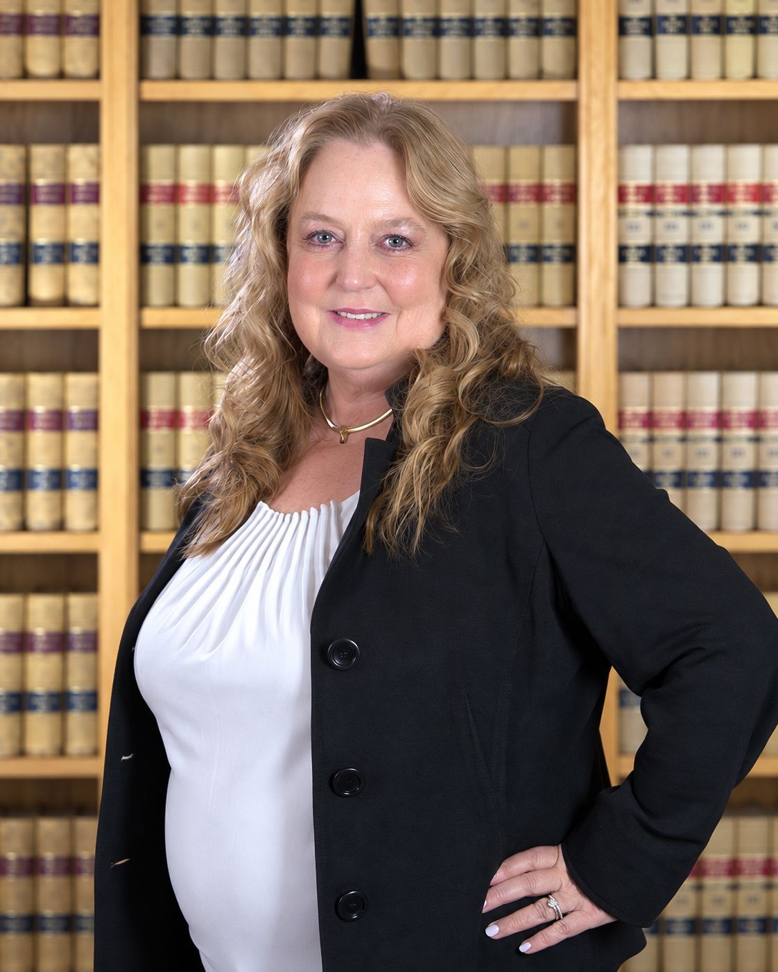 Portrait of a smiling woman in a black blazer and blue top against a teal backdrop