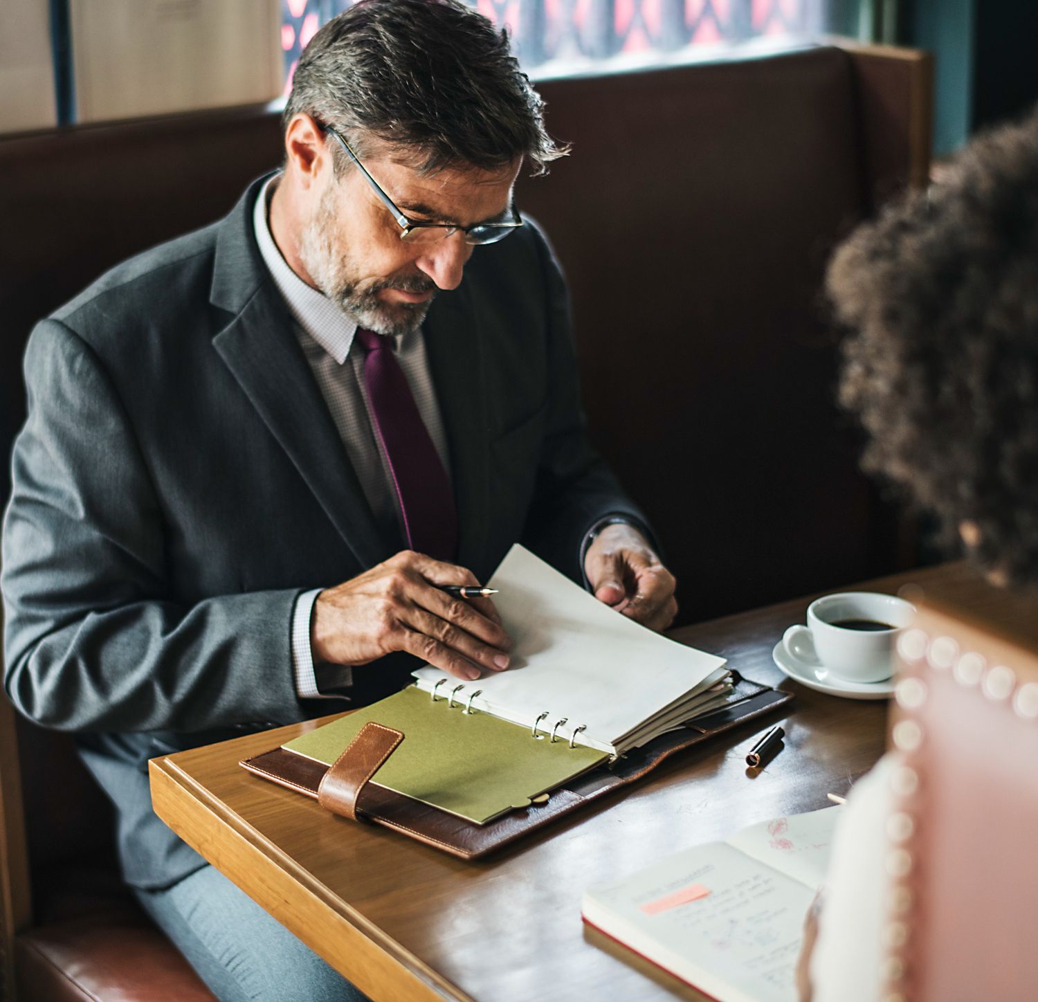 Two people review paperwork and sign a document beside a small building model on a desk