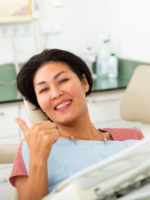 A woman is giving a thumbs up while sitting in a dental chair.