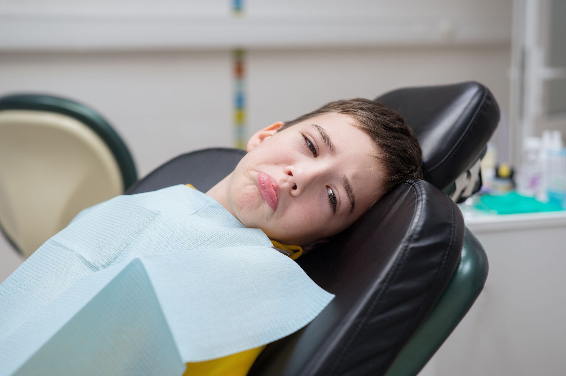 A young boy is laying in a dental chair with a towel around his neck.