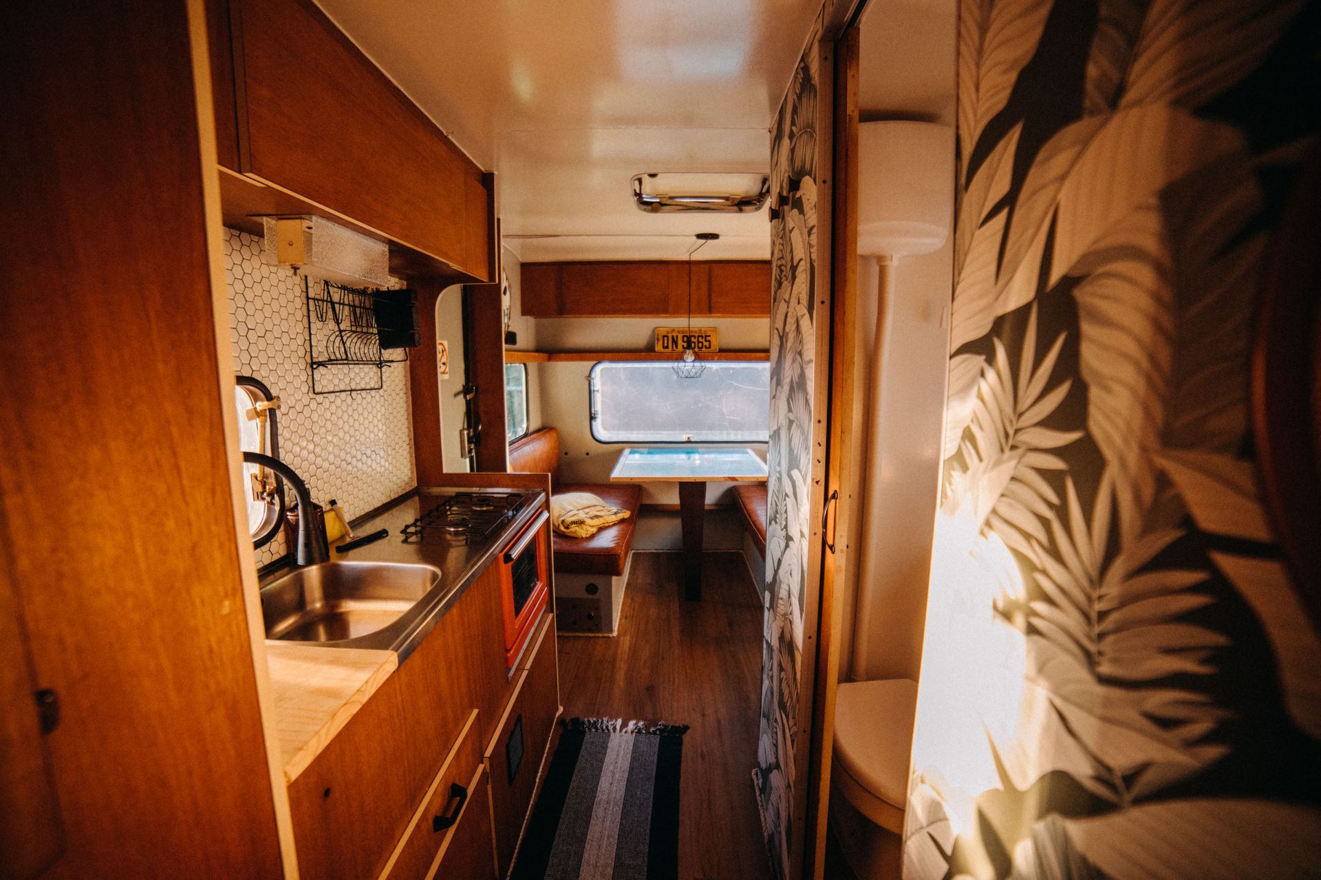 Narrow camper van interior with wood cabinetry, a kitchenette, and a bed by the window.